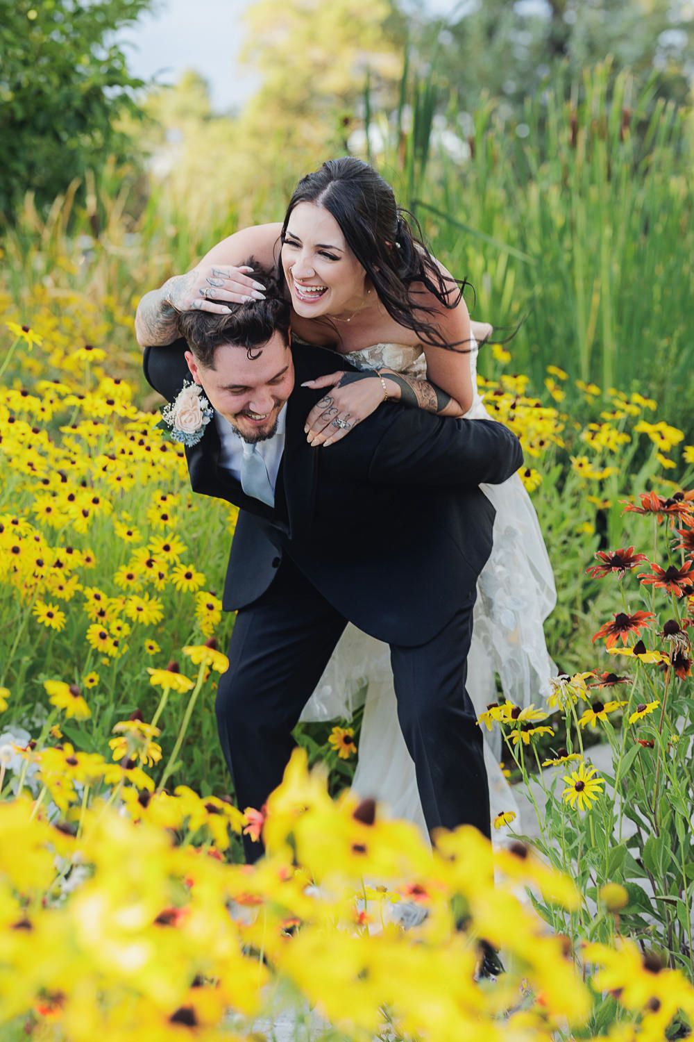 A couple shares joyful laughter together in a vibrant meadow filled with yellow wildflowers and tall green grass.