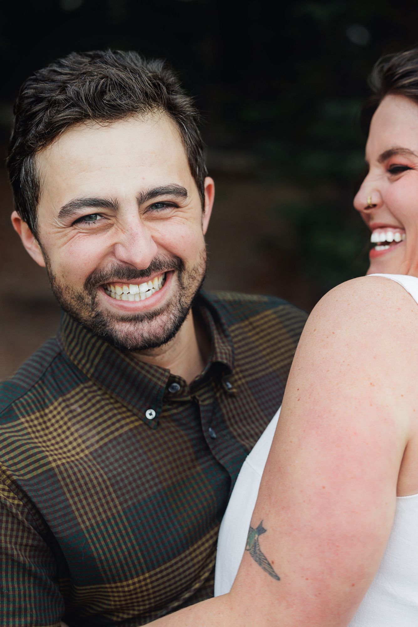 A joyful couple sharing a candid laughing moment together, with one wearing a plaid shirt and the other in white.