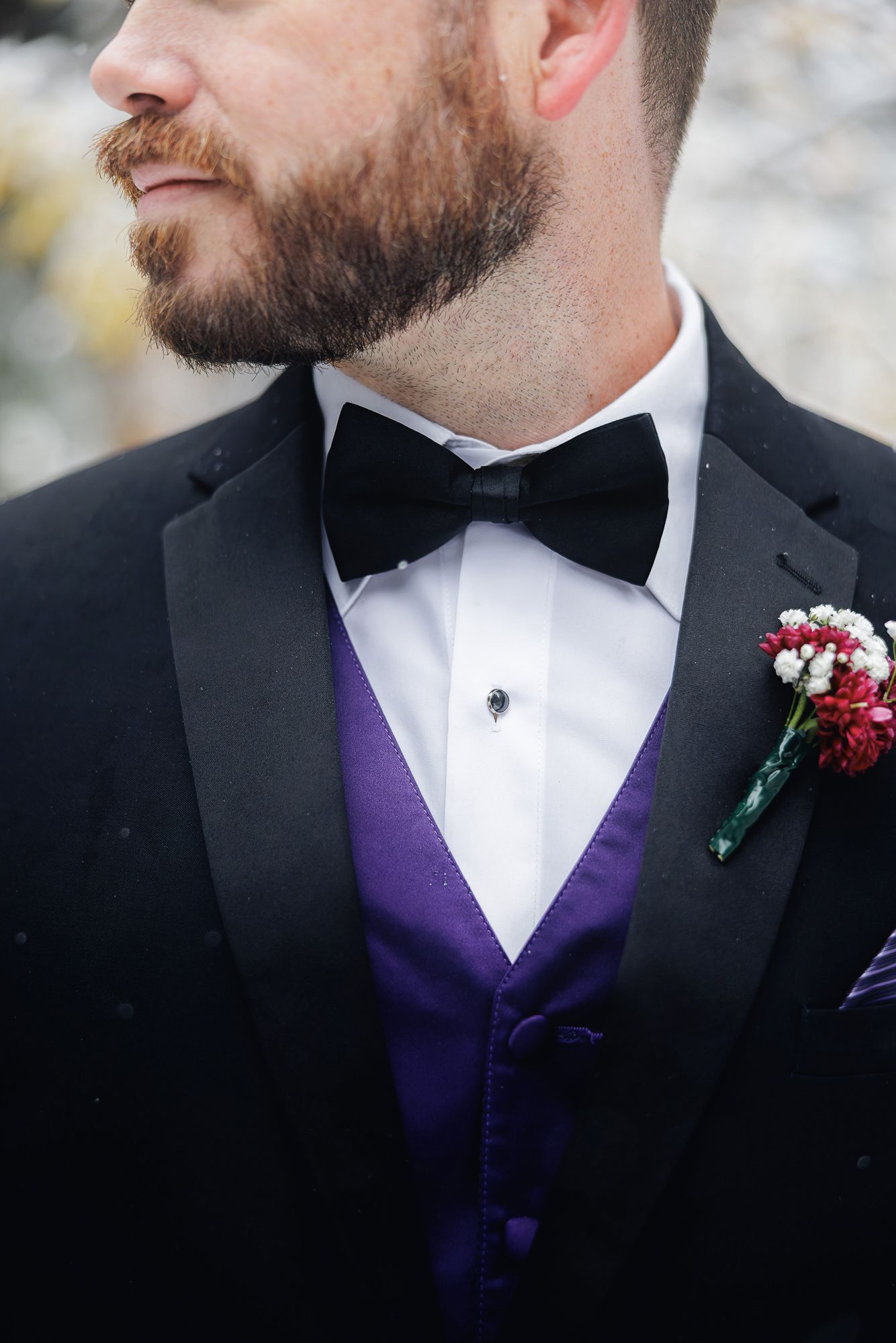 Close-up details of formal attire showing a black tuxedo with purple vest and red boutonniere.