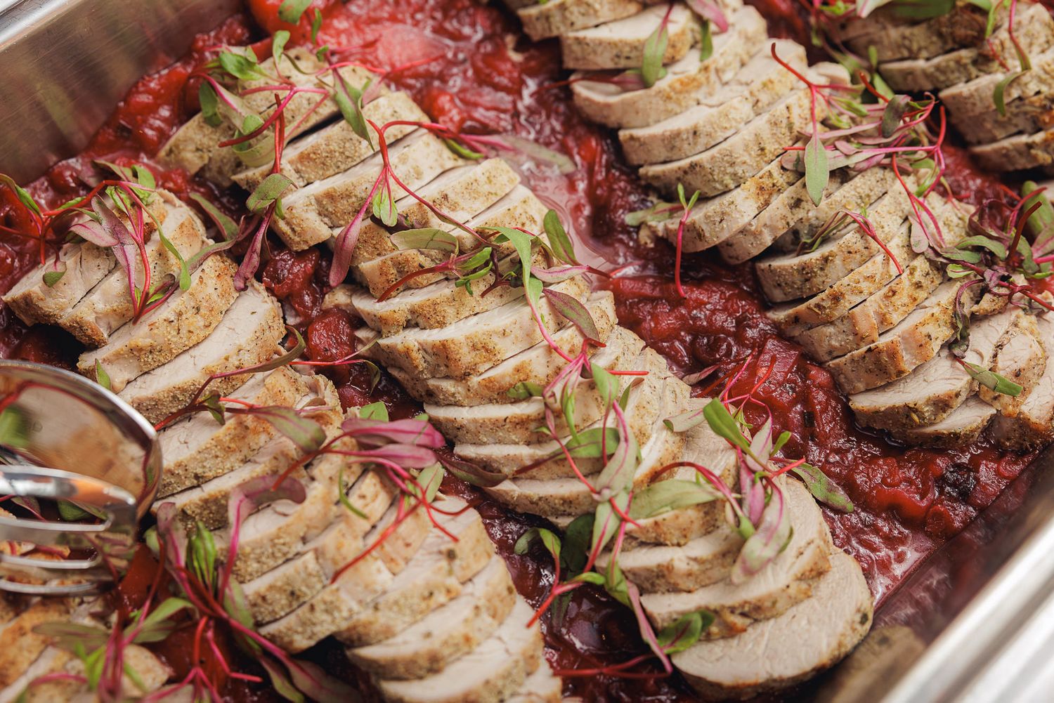 Sliced chicken breast arranged over a bed of red cabbage and garnished with fresh herbs in a catering pan.