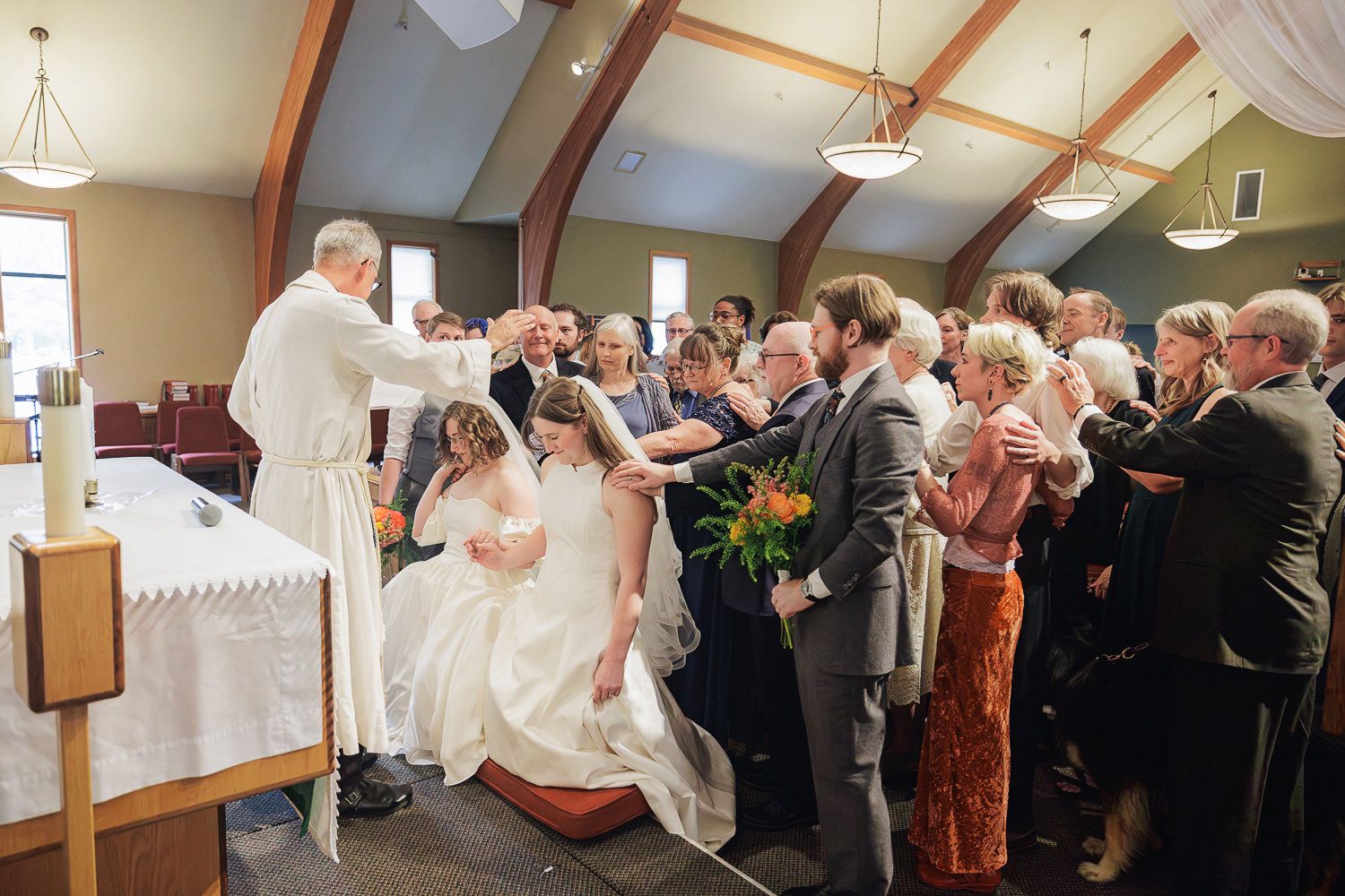 Wedding guests dance together in a line during a reception celebration in an indoor venue with exposed beams.