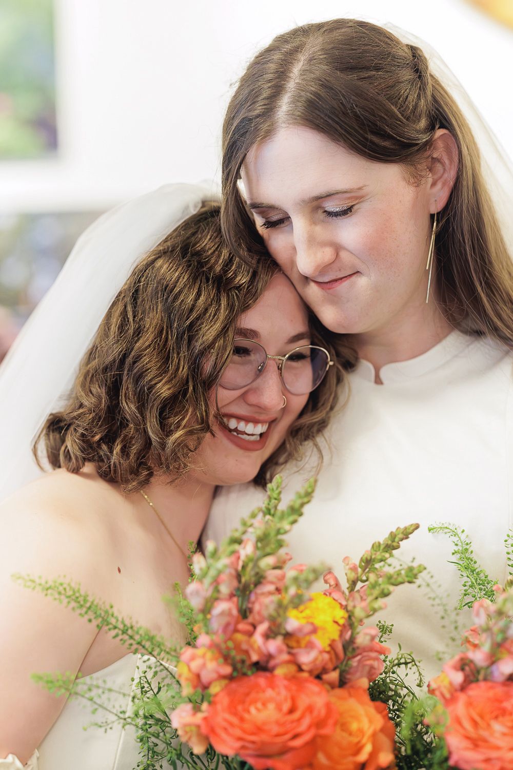 Two people share an intimate moment while holding a vibrant bouquet of orange roses and greenery.
