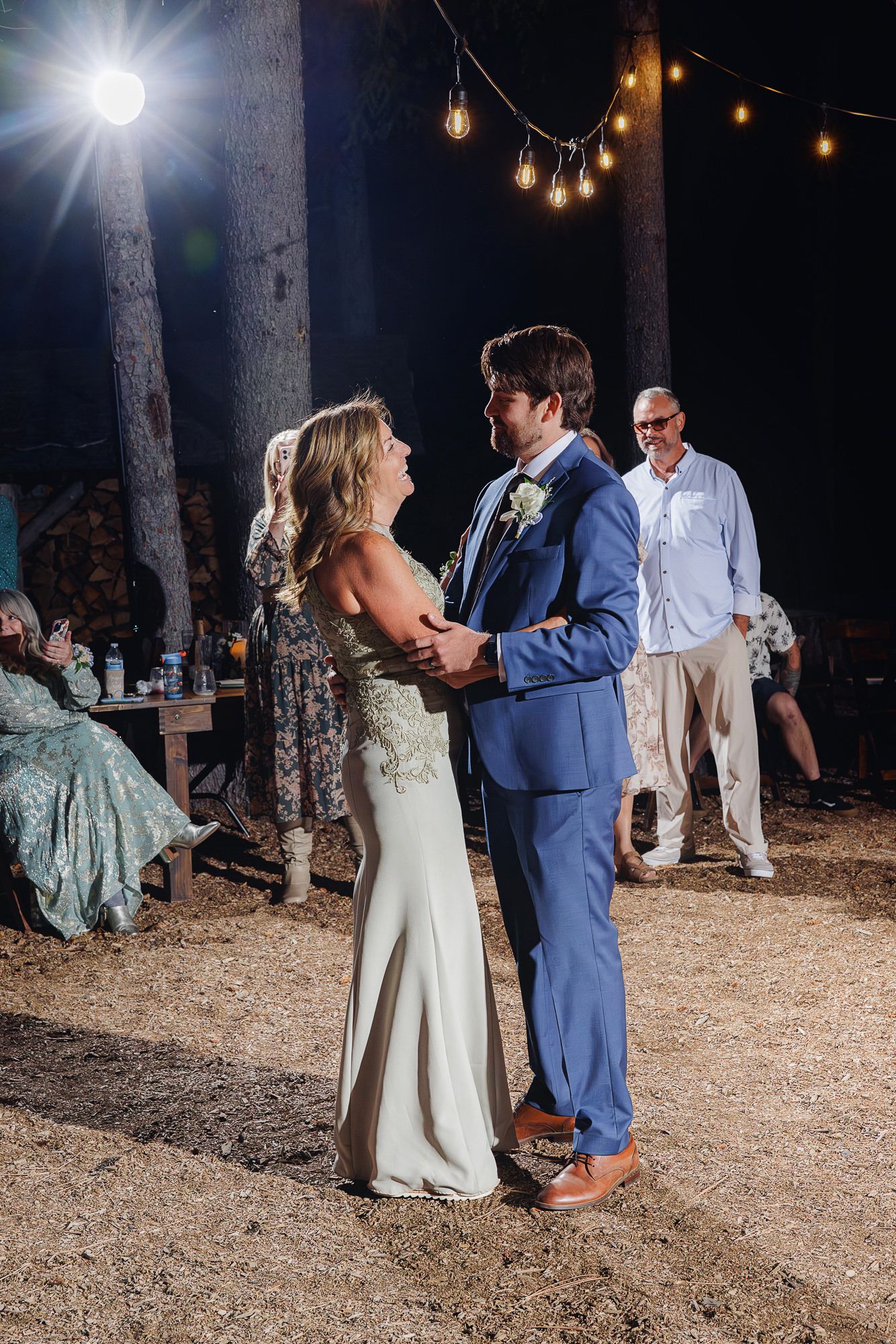 A romantic first dance sequence at an outdoor evening wedding reception under string lights in a rustic woodland setting.