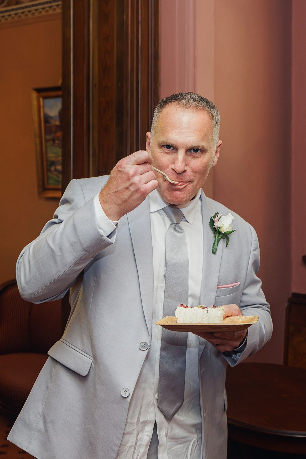 A person in a light gray suit demonstrates eating cake in a series of sequential photos captured indoors.