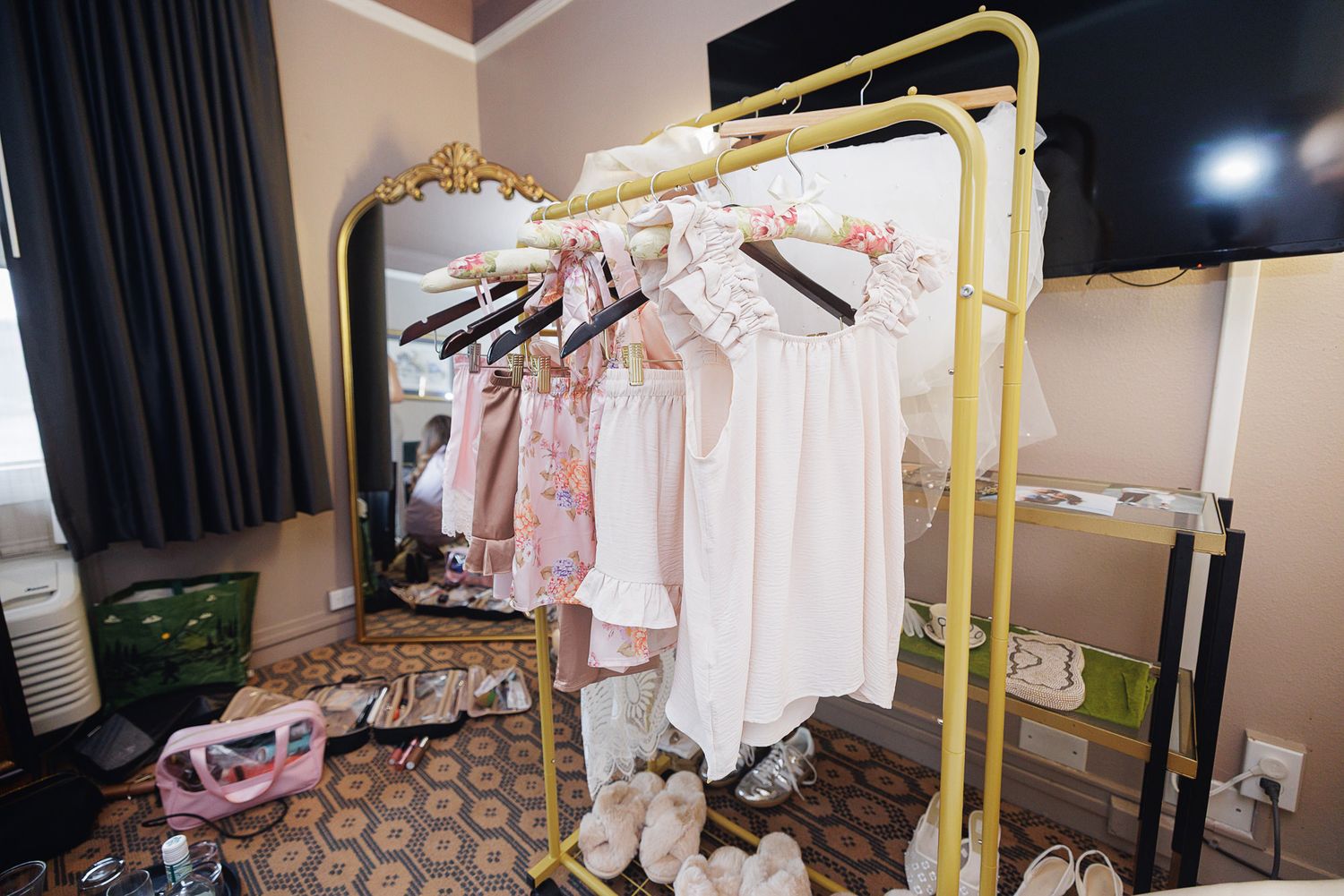 A yellow clothing rack with pink and white dresses in a decorated room with shoes and a mirror.