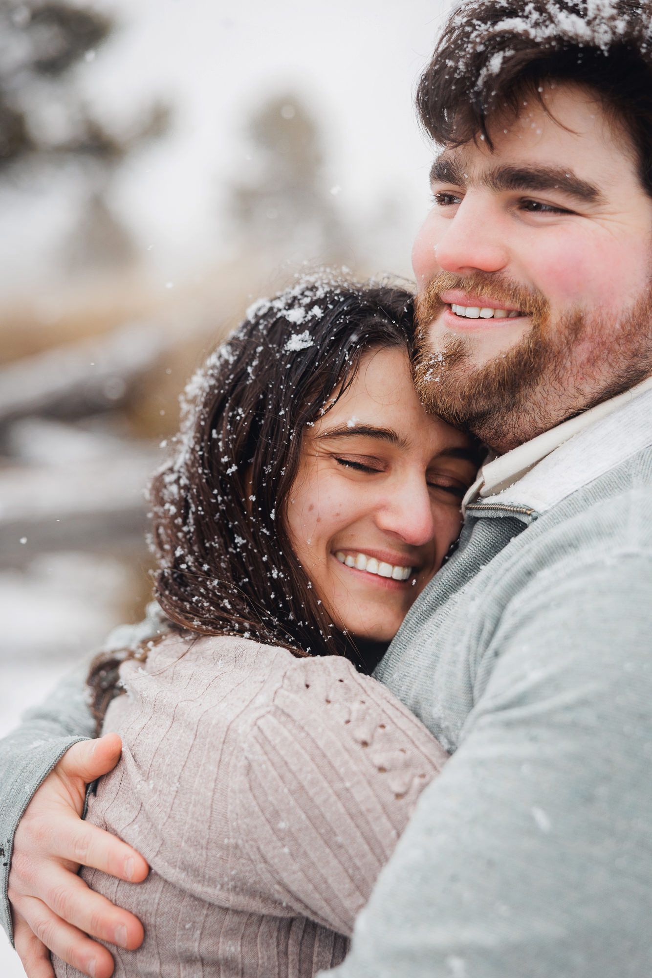A couple embraces in the snow, sharing tender moments while snowflakes fall around them.