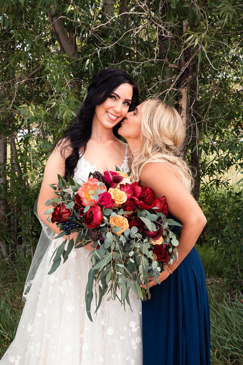 A bouquet of red and orange roses with eucalyptus greenery is held during a wedding outdoors.