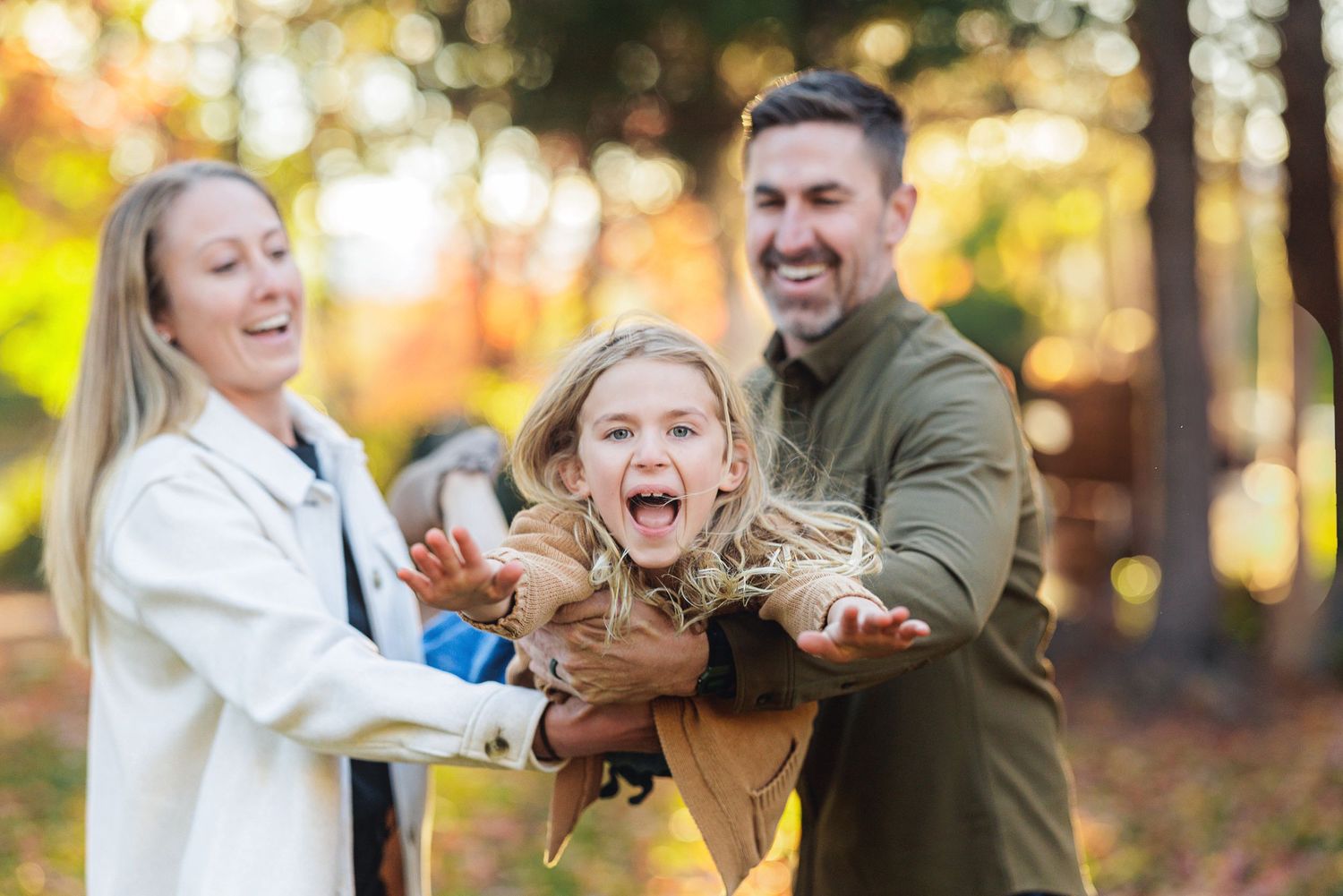 Playful family moment outdoors with child laughing in autumn forest.