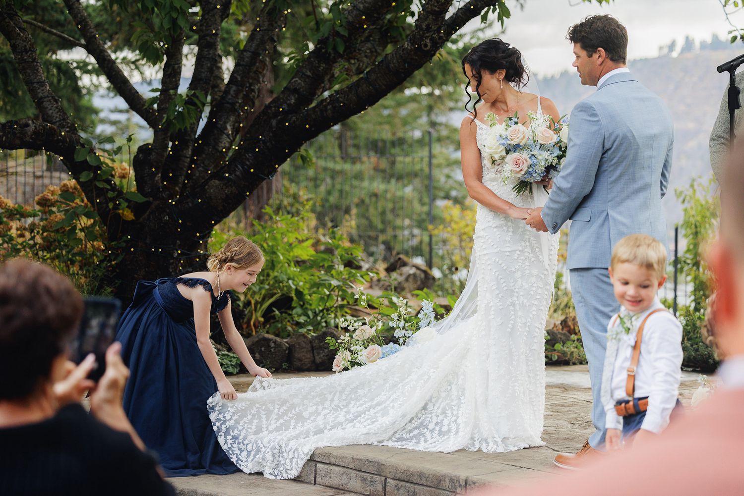 Wedding celebration in a lush garden setting with guests gathered under trees.