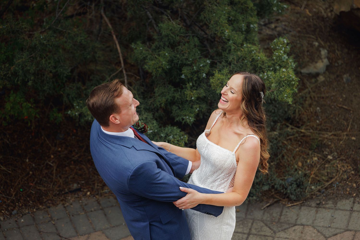 A couple shares a joyful moment together outdoors, laughing while dressed in formal wedding attire.