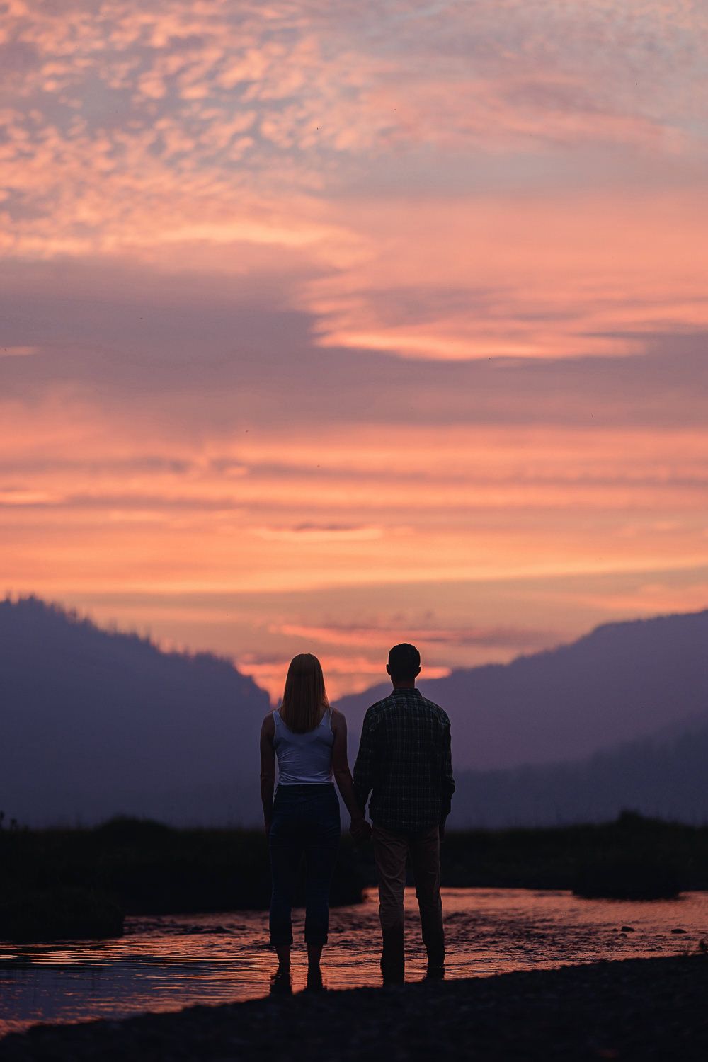 Silhouettes of people standing together against a vibrant pink and purple sunset over mountains and water.