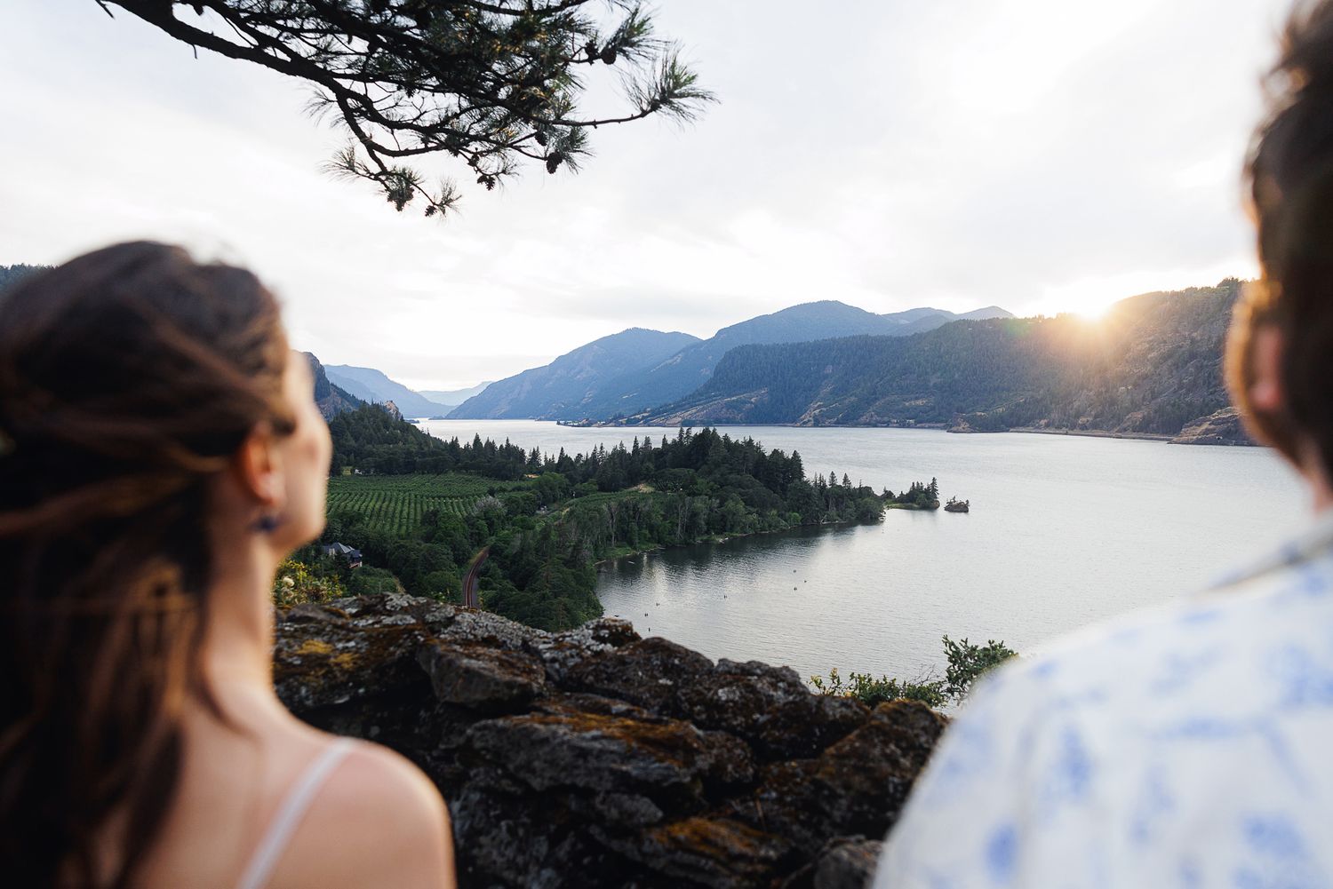 Couple gazing at stunning Columbia River Gorge sunset with lush green islands and mountain backdrop.