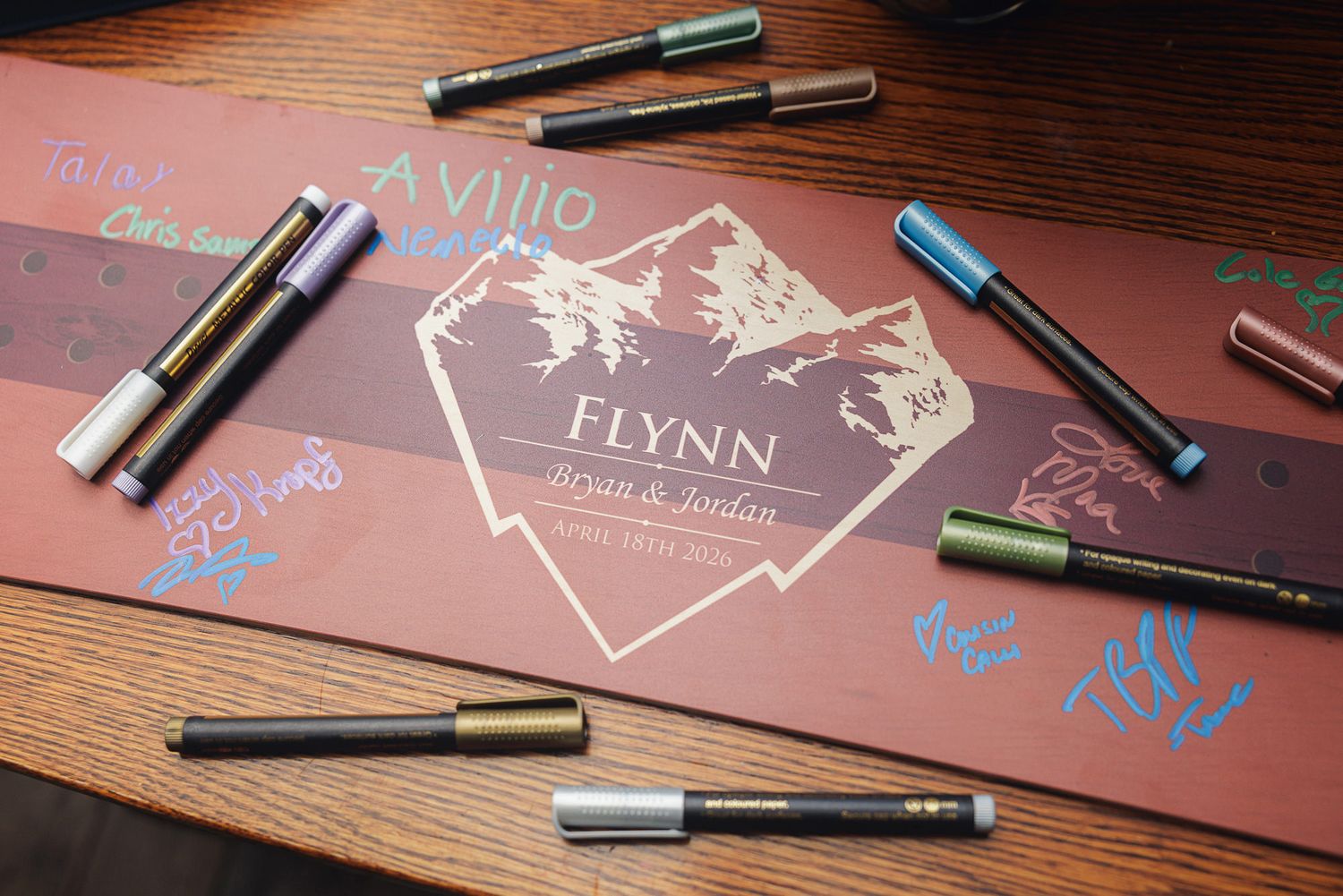 Wedding guest book sign with Flynn family name, Bryan and Jordan, surrounded by colorful metallic pens on a wooden table.