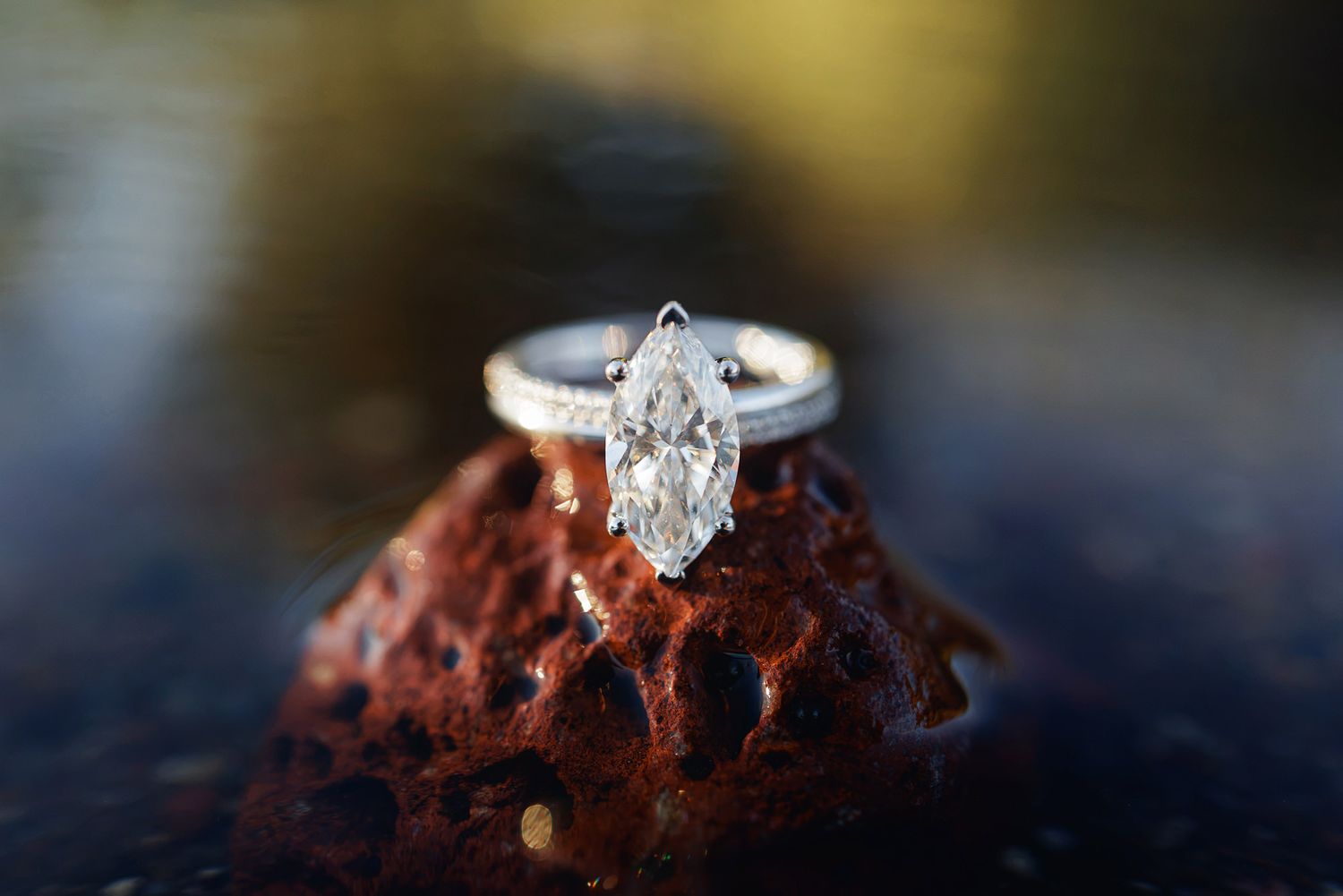 A stunning marquise-cut diamond solitaire engagement ring displayed on a rustic red rock surface.