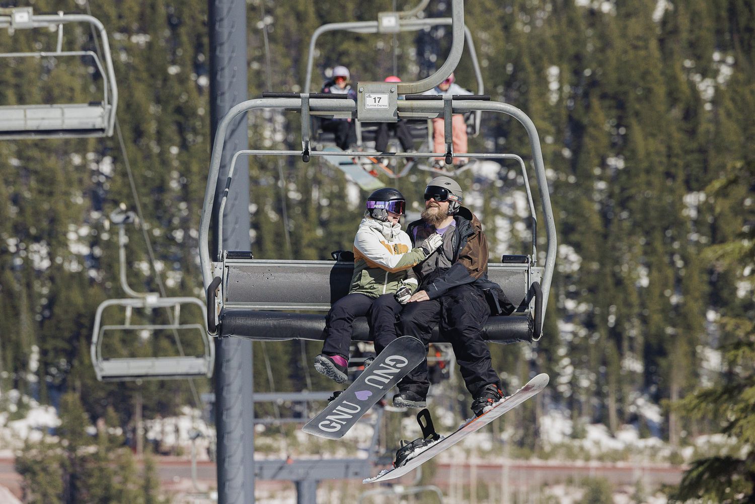 Two people riding on a ski lift chair in a snowy forest.