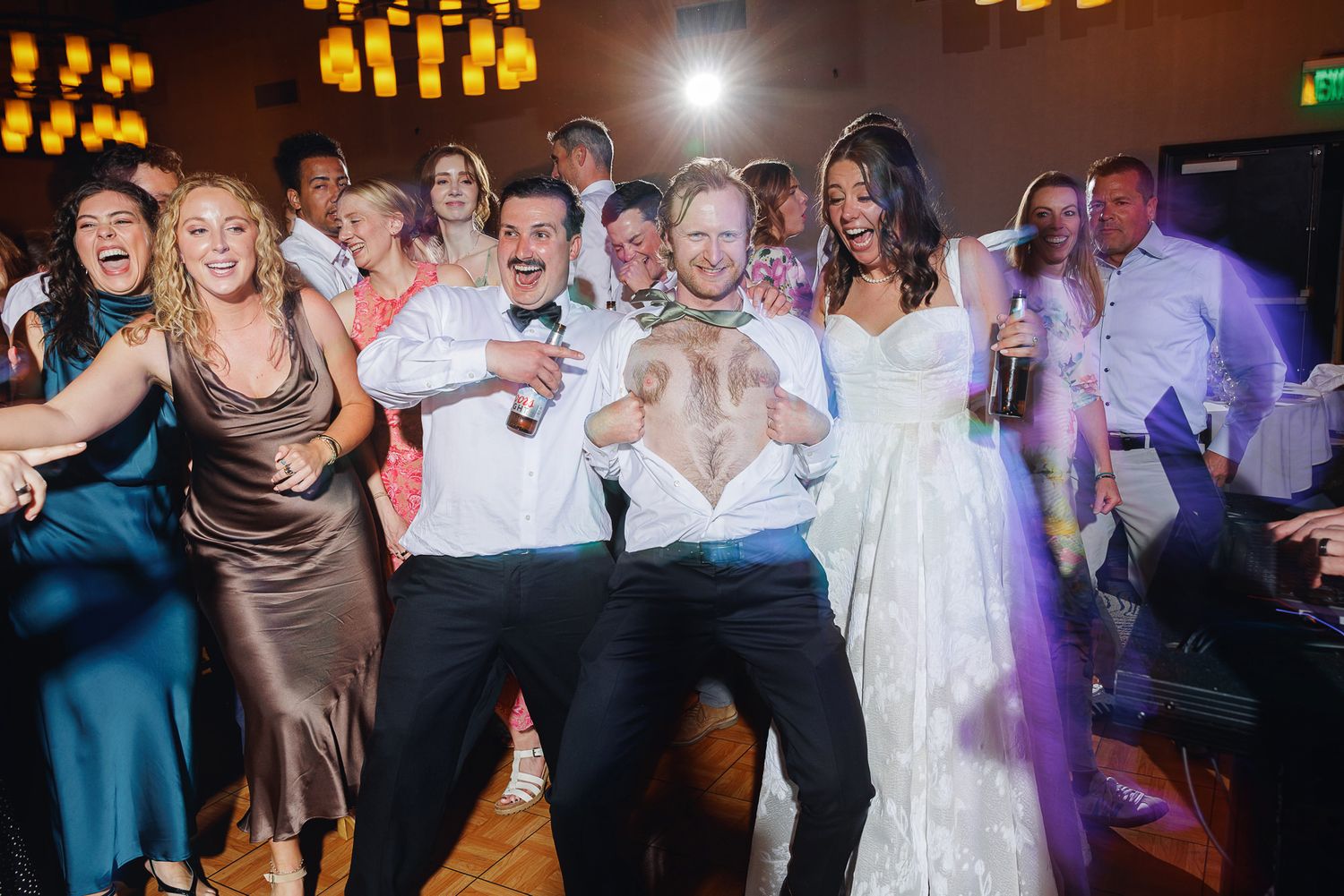 Joyful wedding reception dance floor with bride in white gown, groom, and guests celebrating together.