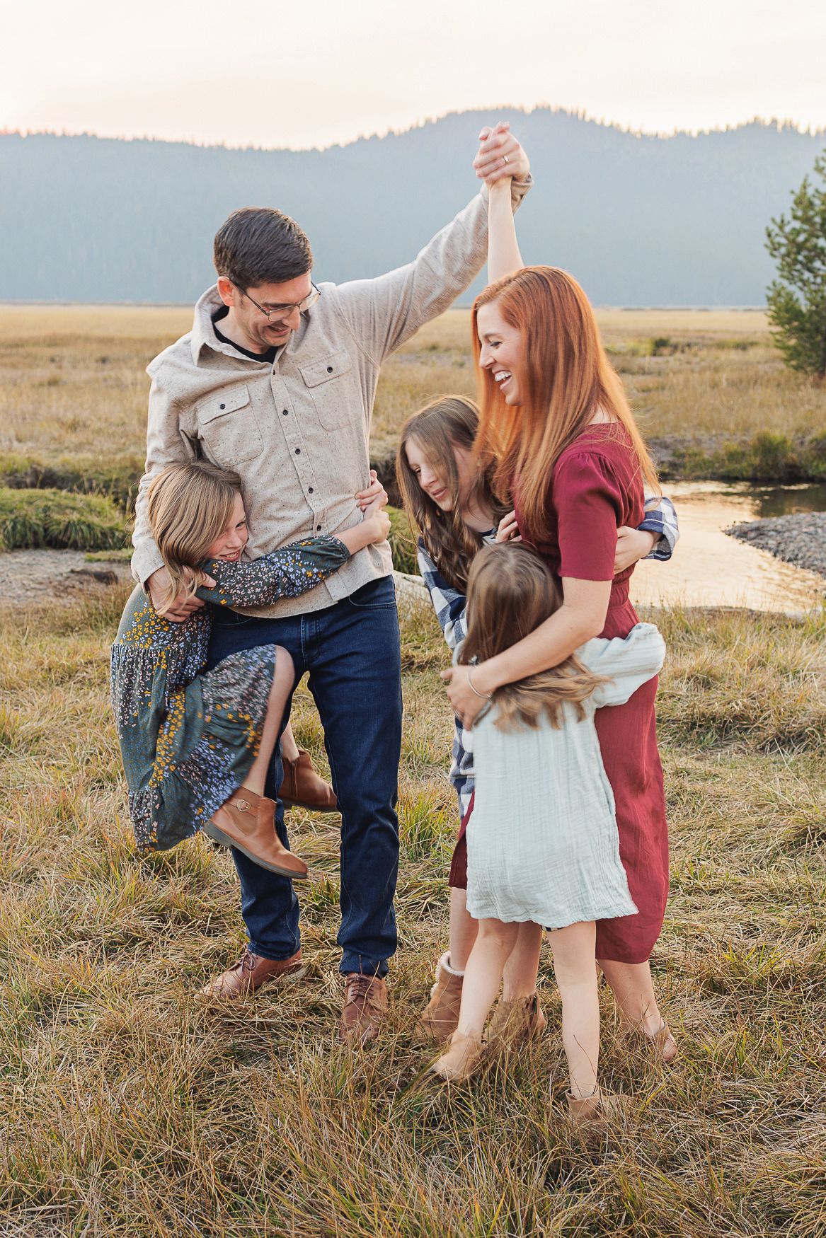 Family dancing together in a mountain meadow at sunset.