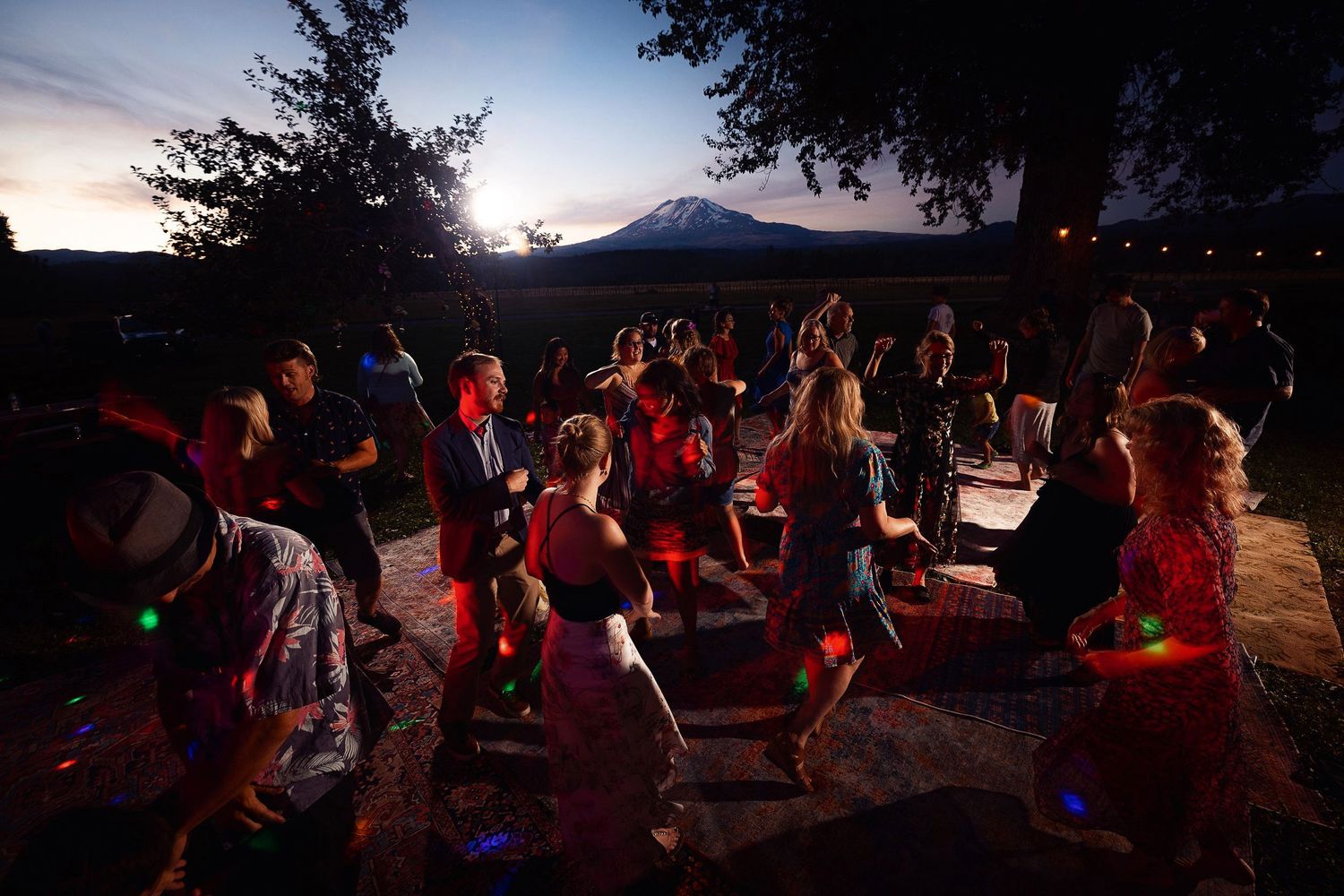Crowd dancing at an outdoor evening celebration with colorful lighting.