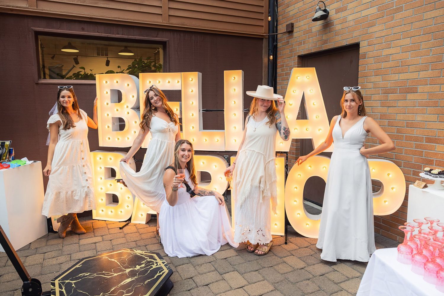 Group photo in front of large illuminated BELLA BAMBINO letters at outdoor event.