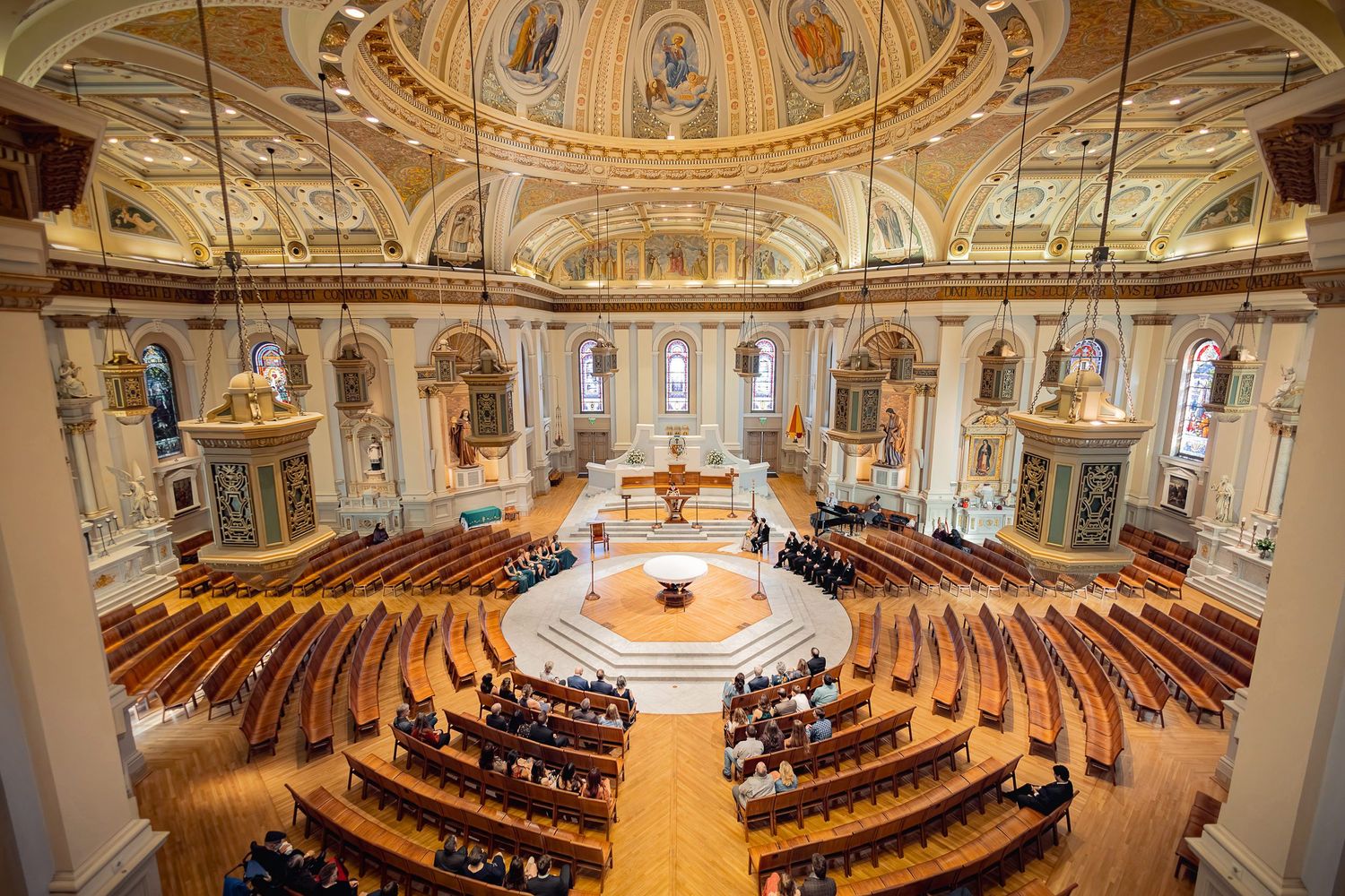 Interior view of an ornate cathedral with a circular layout and golden domed ceiling during a ceremony.