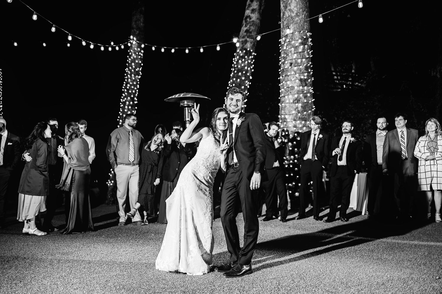 A black and white wedding reception scene at night with string lights and palm trees illuminating the outdoor dance floor.