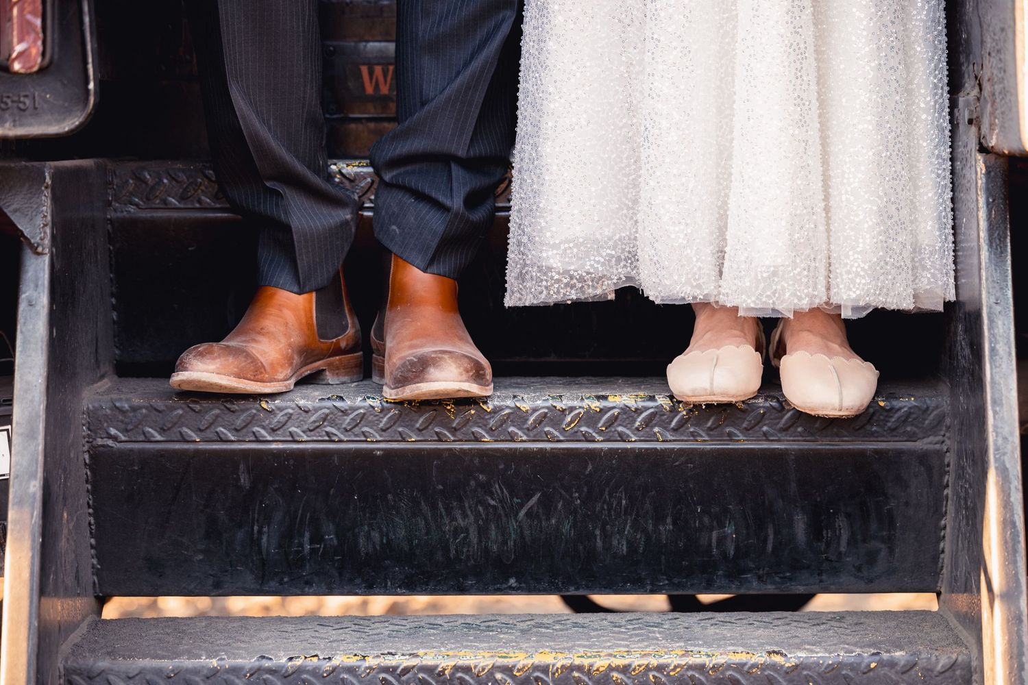 A close-up of brown leather dress shoes and pink ballet flats standing on metal stairs.
