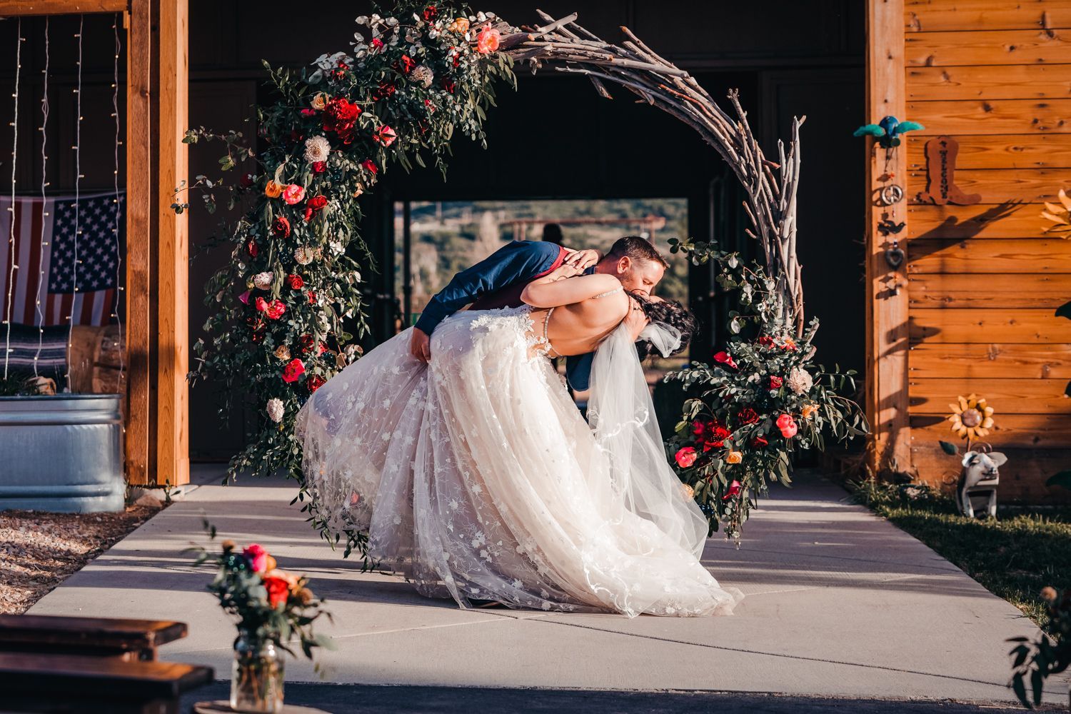 A decorative floral arch with red roses frames a romantic moment on a wooden porch.