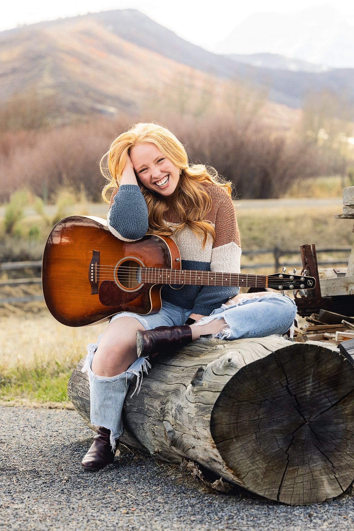 A candid portrait with an acoustic guitar sitting on a log against a mountain backdrop.