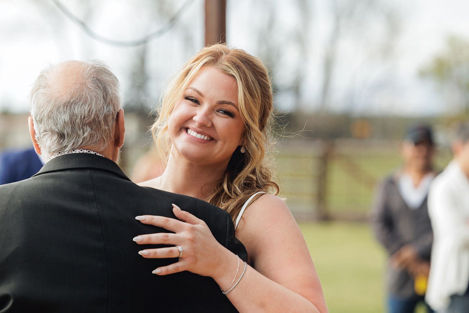 A smiling woman in a black dress shares a warm dance with an older man at an outdoor event.