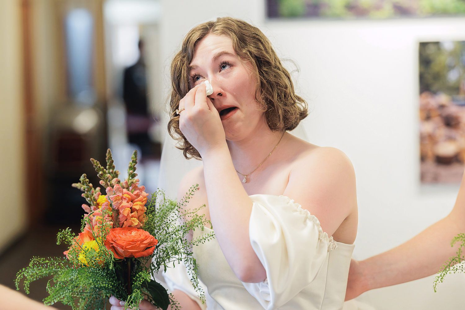 A bride in a white wedding dress laughs joyfully while holding a vibrant orange and coral floral bouquet.