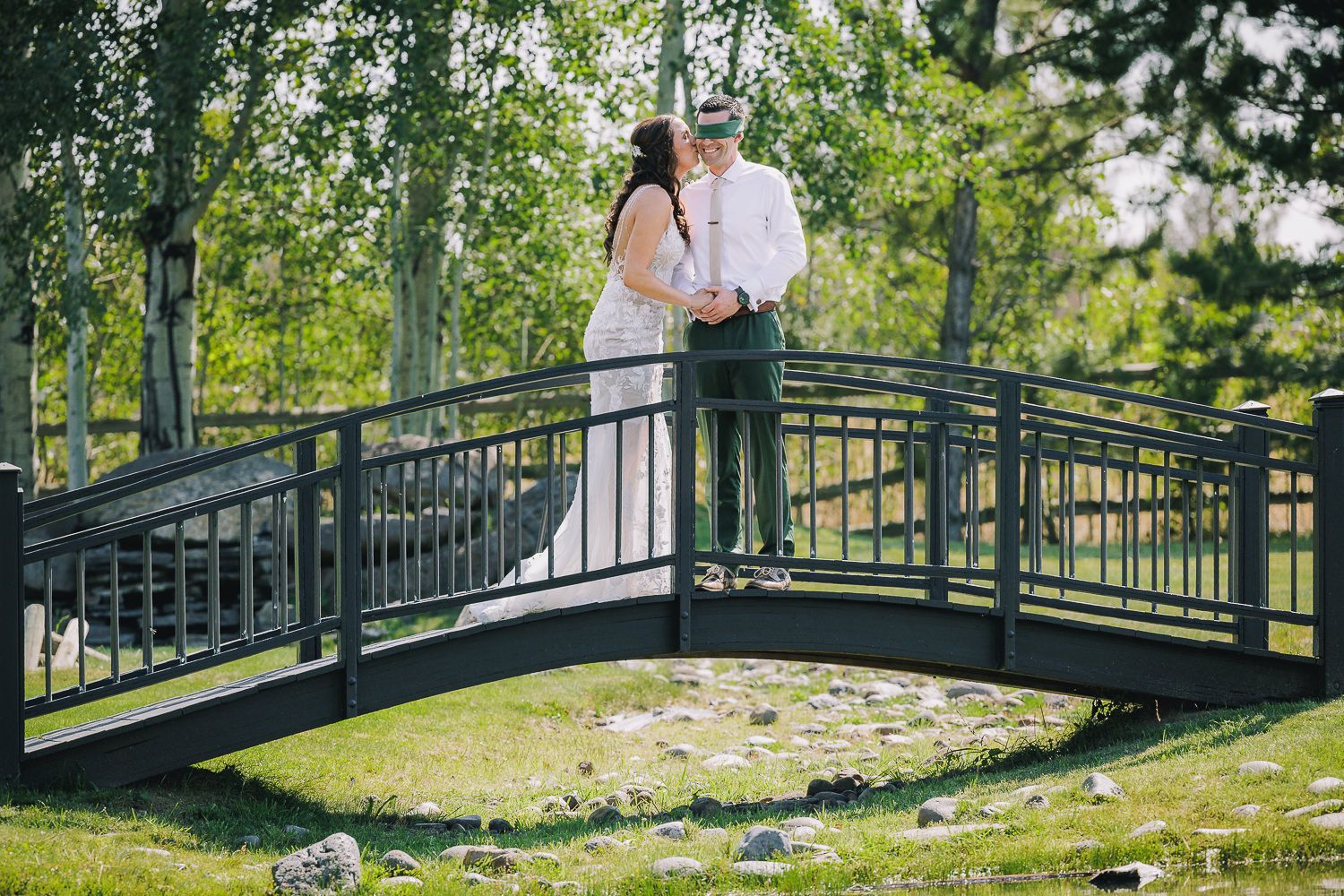 A couple shares an intimate moment on a charming black garden bridge surrounded by lush summer greenery.