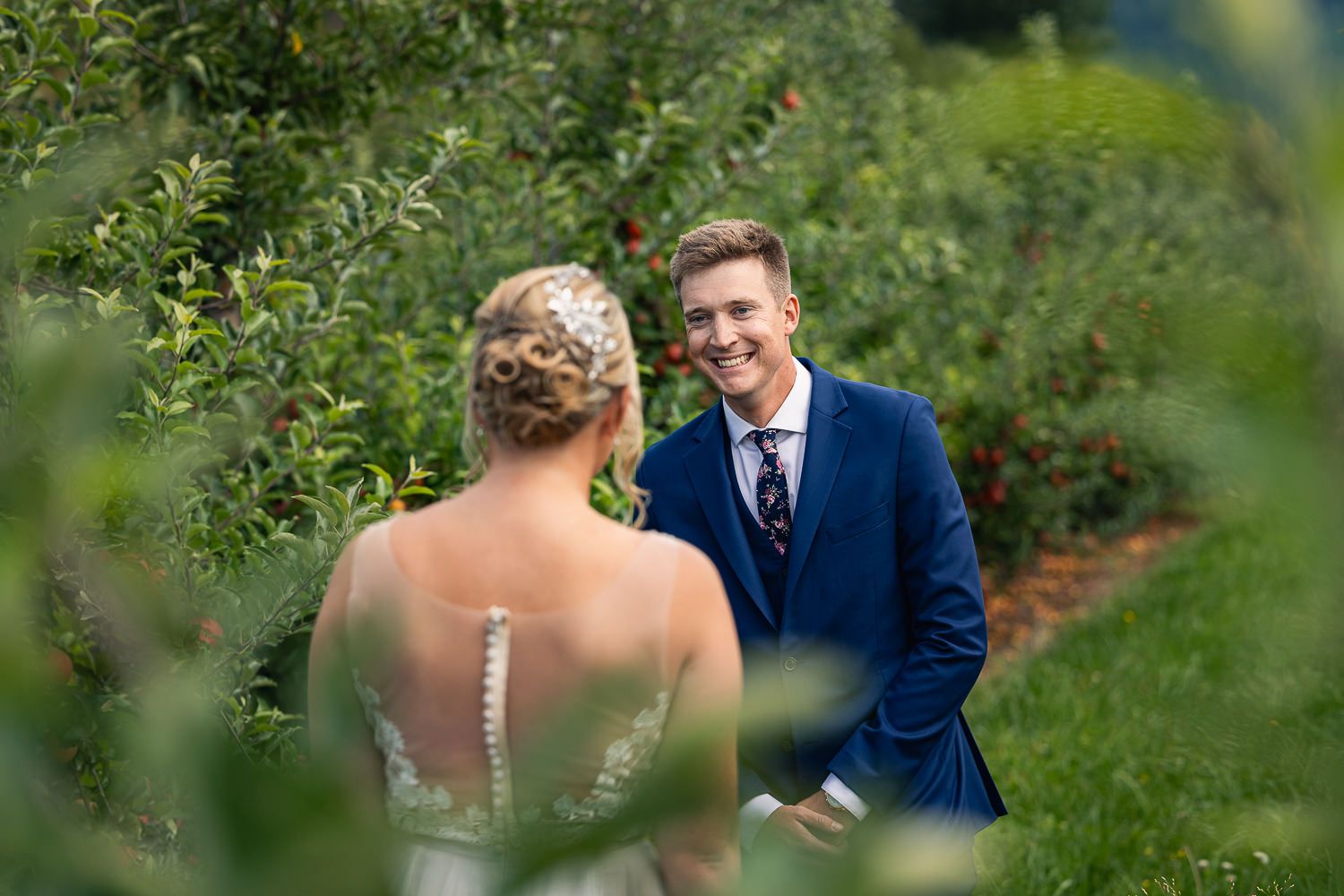 A couple shares a joyful moment together in an orchard setting framed by green foliage on their wedding day.