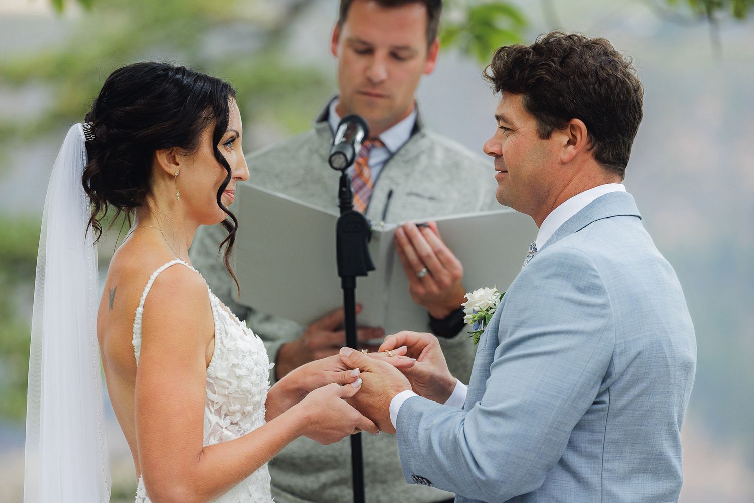 A couple exchanges rings during their outdoor wedding ceremony with an officiant present.