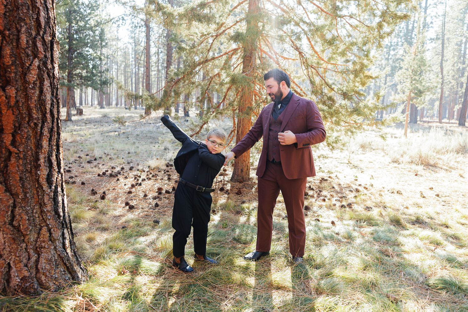 People enjoying a playful moment in a sunlit forest with tall pine trees.