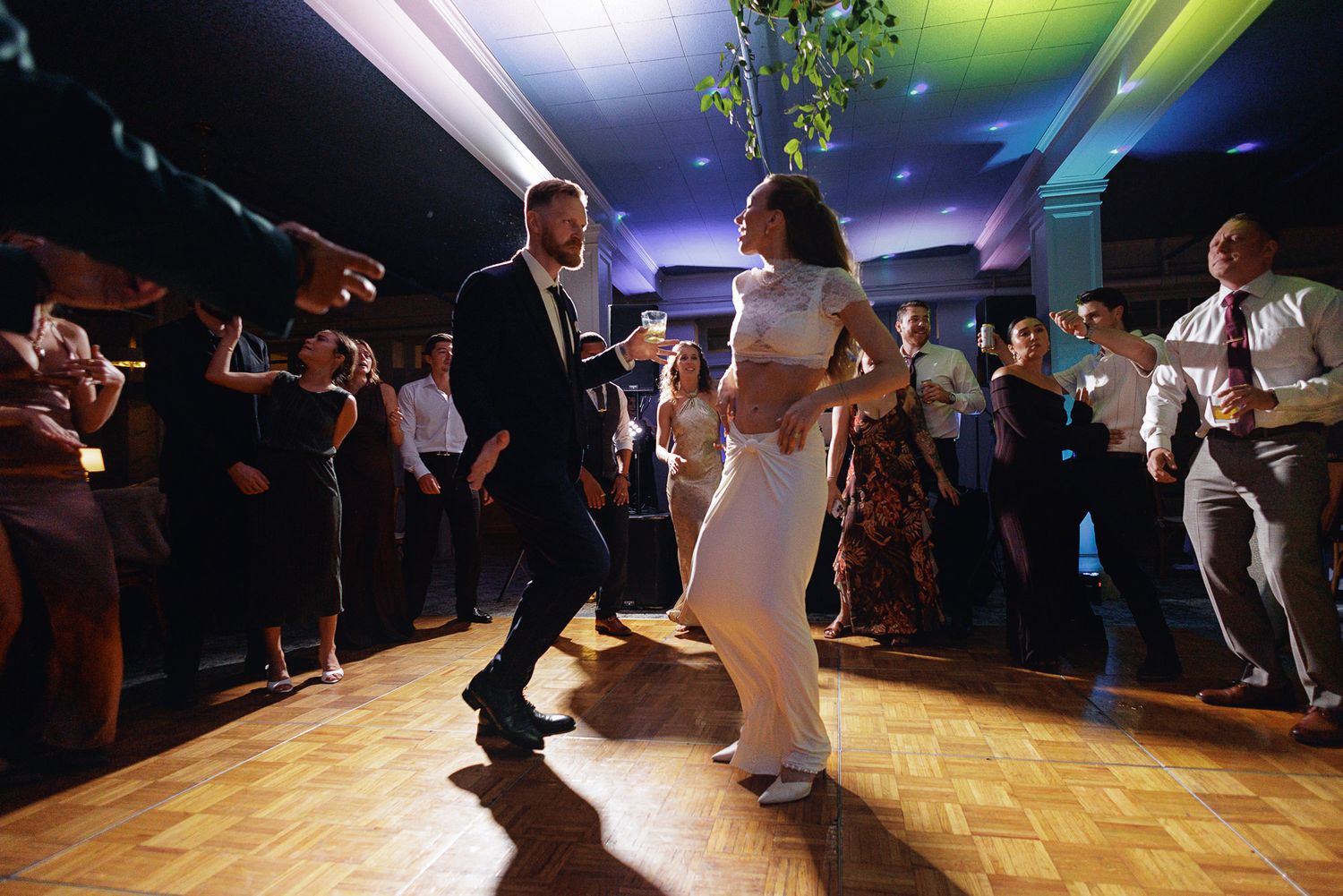 Couple sharing first dance at wedding reception on wooden dance floor surrounded by celebrating guests.