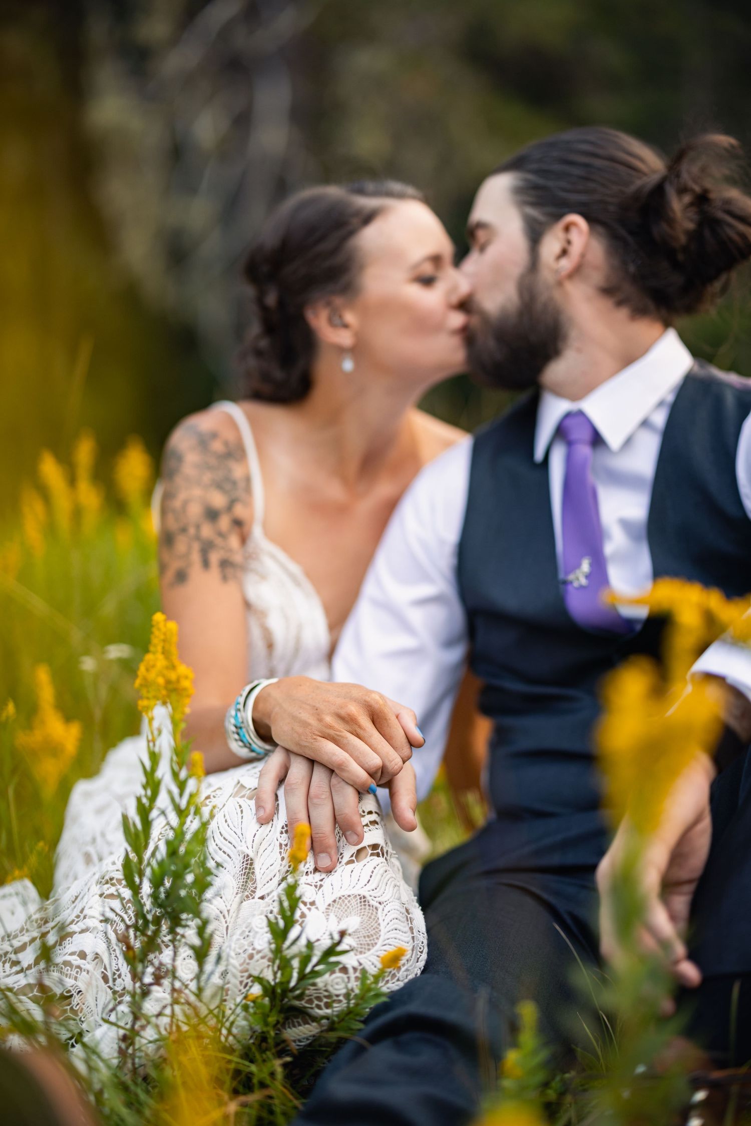 A romantic kiss shared between newlyweds surrounded by yellow wildflowers during their outdoor wedding photoshoot.
