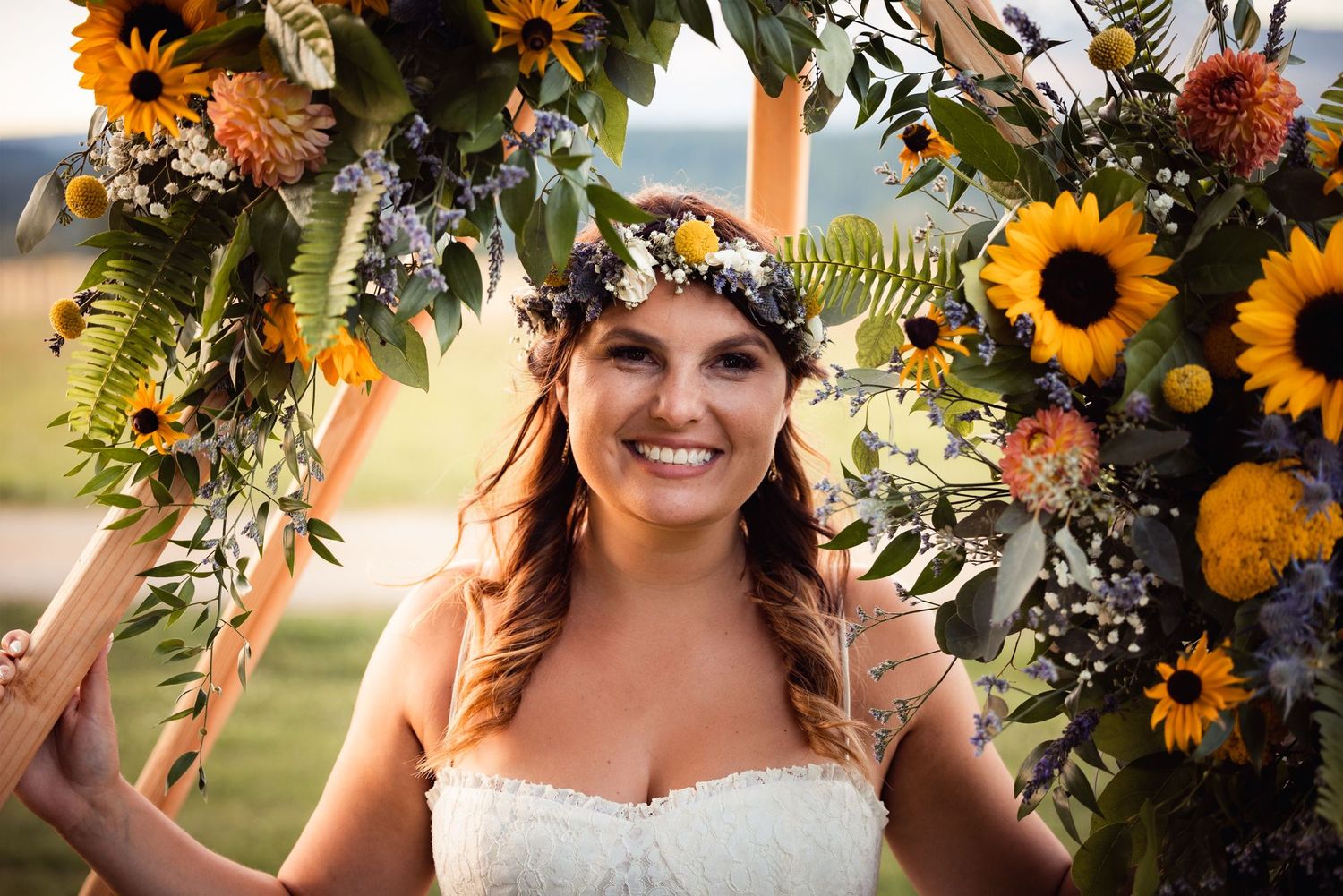 A wedding scene under a floral arch decorated with vibrant sunflowers, greenery and orange blooms in an outdoor setting.