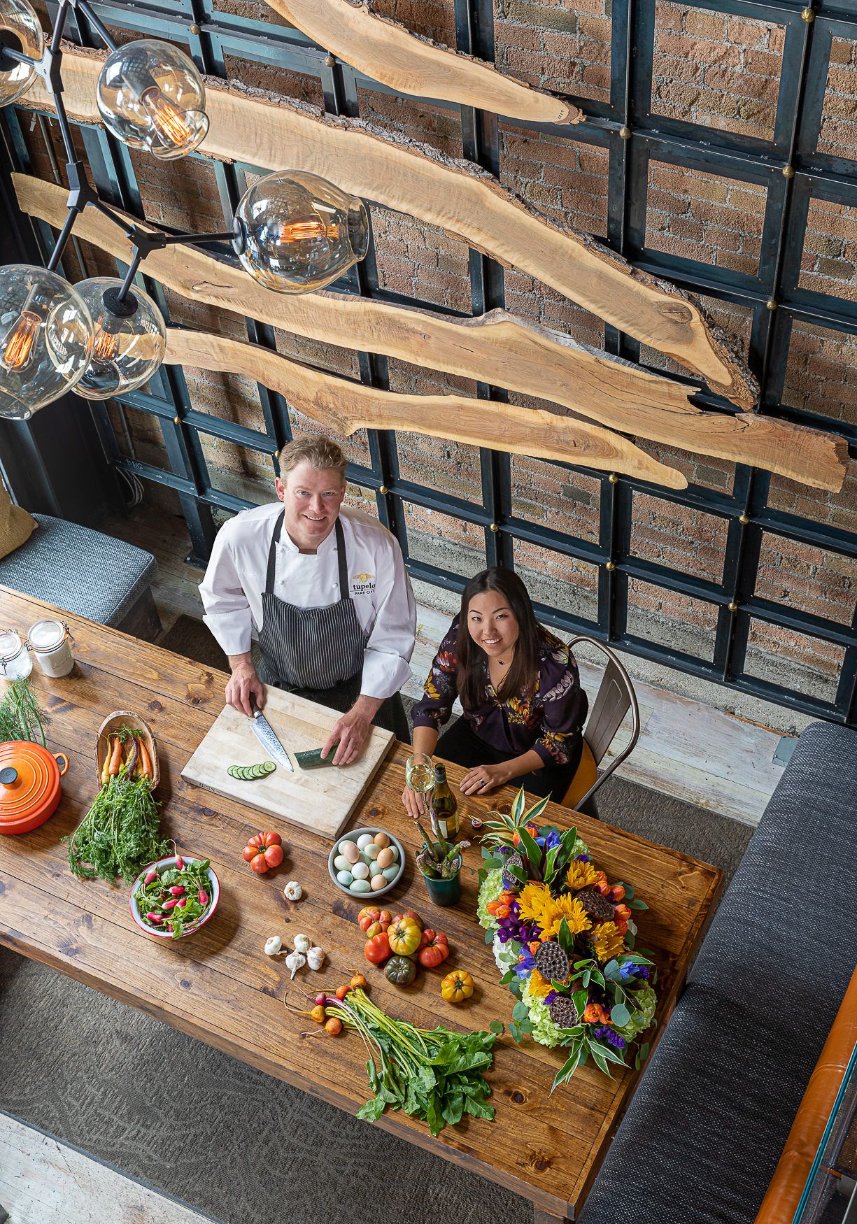 Overhead view of food preparation on rustic wooden table with hanging pendant lights.