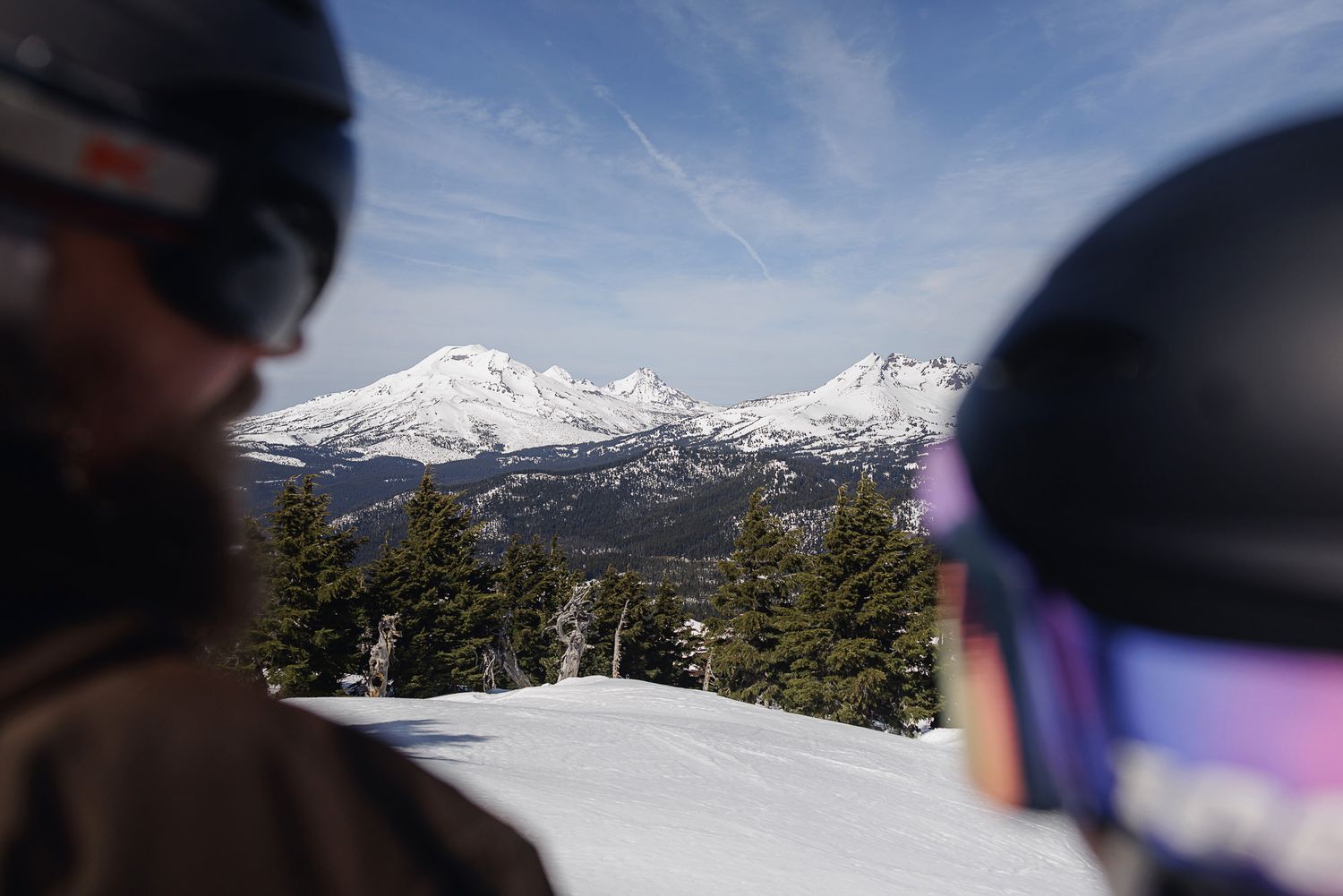 A snowy mountain landscape is visible in the background, with skiers or snowboarders in the foreground.