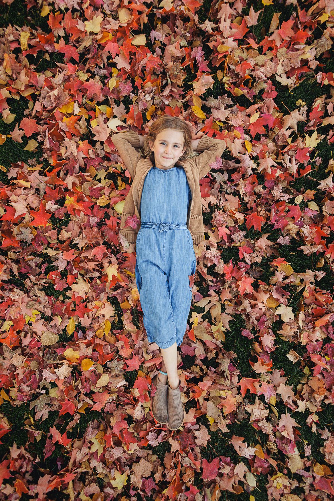 Overhead shot of person laying in vibrant autumn leaves wearing blue jumpsuit.