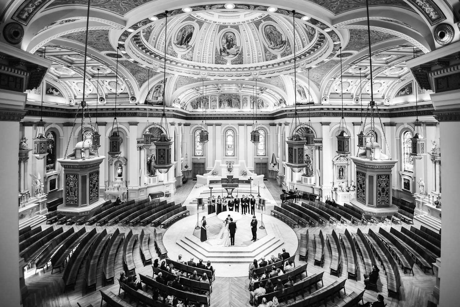 Black and white interior view of an ornate historical church sanctuary with domed ceiling and curved pews around central altar.