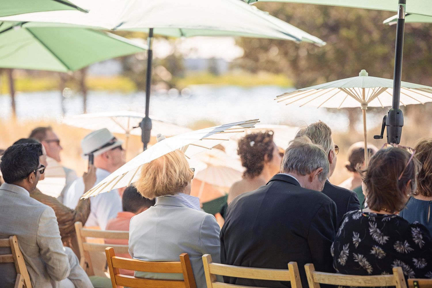 Wedding guests seated under umbrellas at an outdoor reception venue.