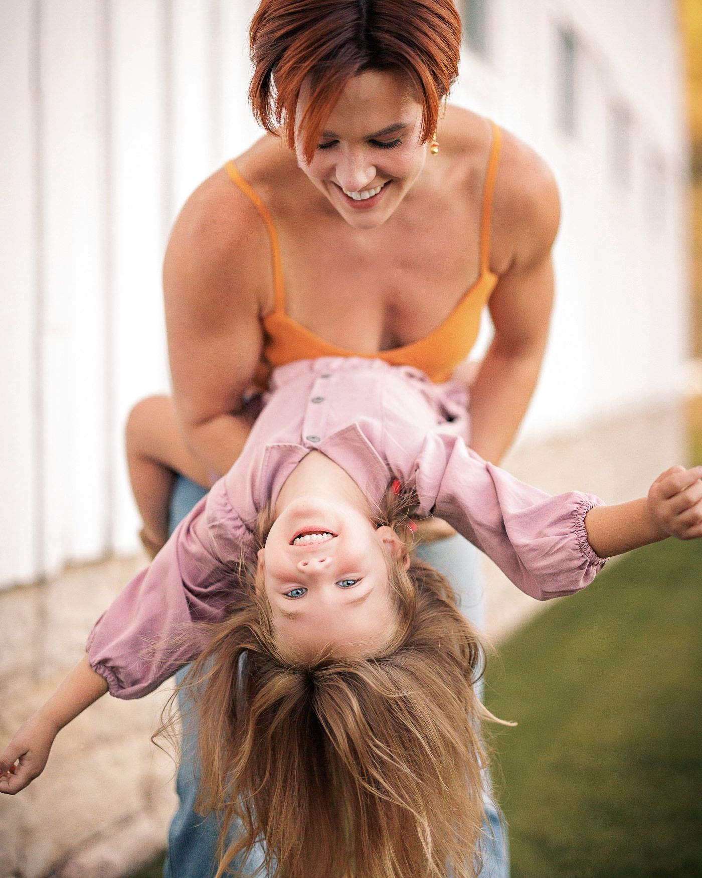 A playful moment captured as a parent holds a laughing child upside down in a bright interior setting.