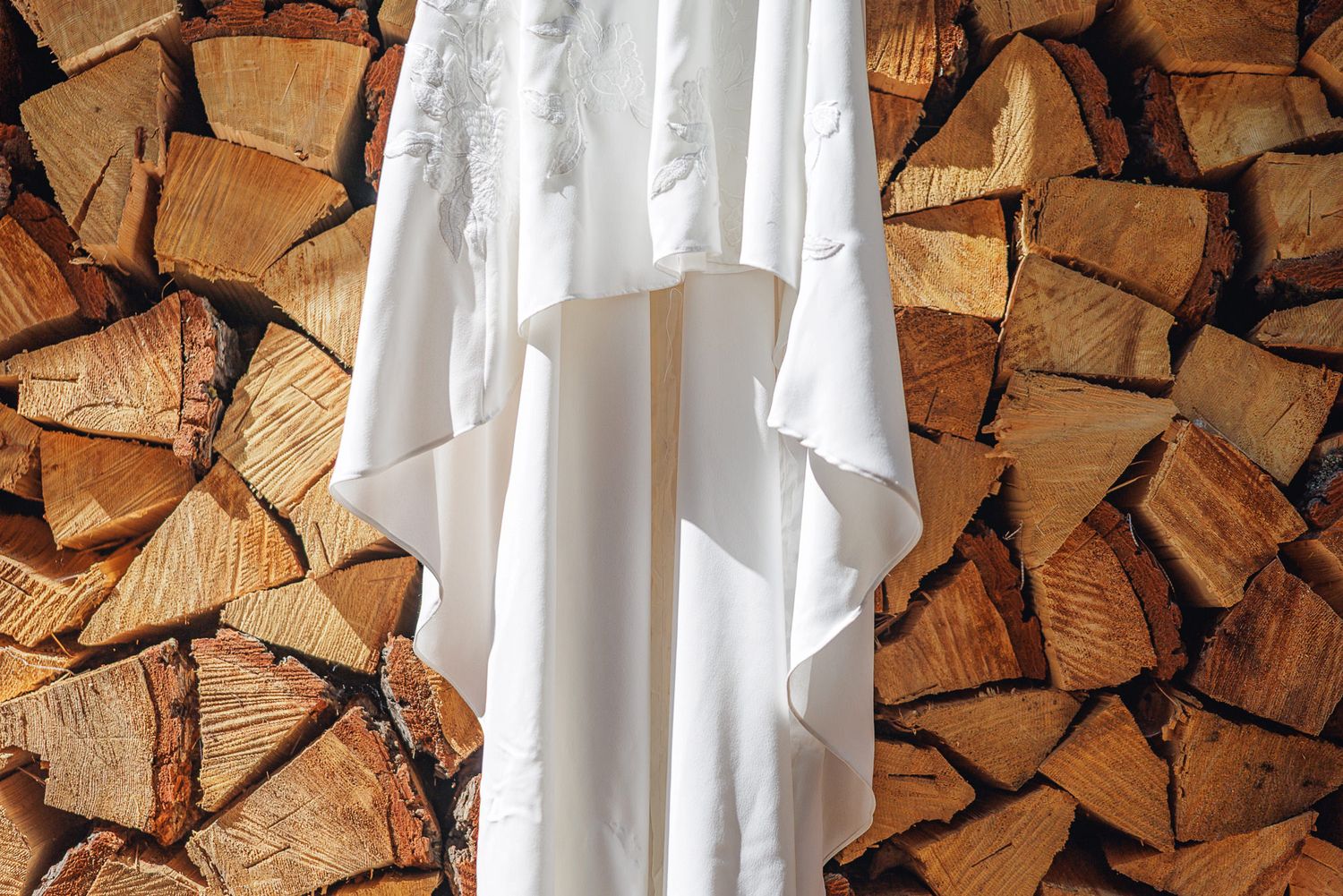 Neatly stacked firewood logs arranged in rows against a white wall create an organized woodpile pattern.