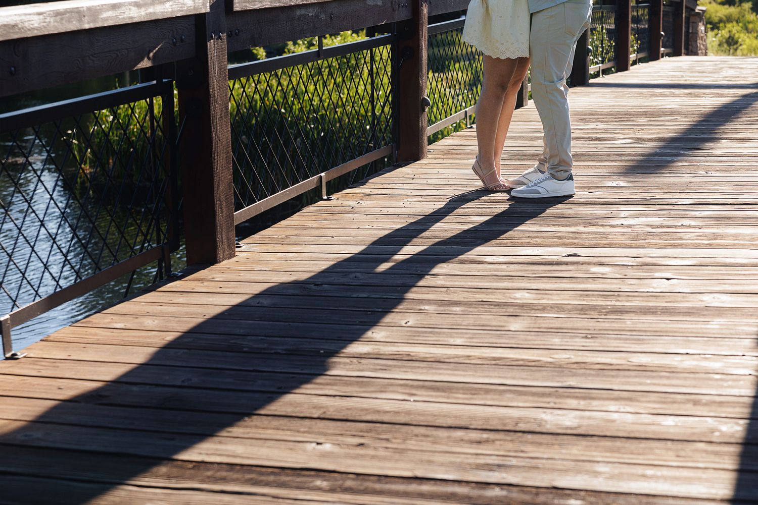 Person walking barefoot on a wooden boardwalk bridge casting a long shadow on sunny day.