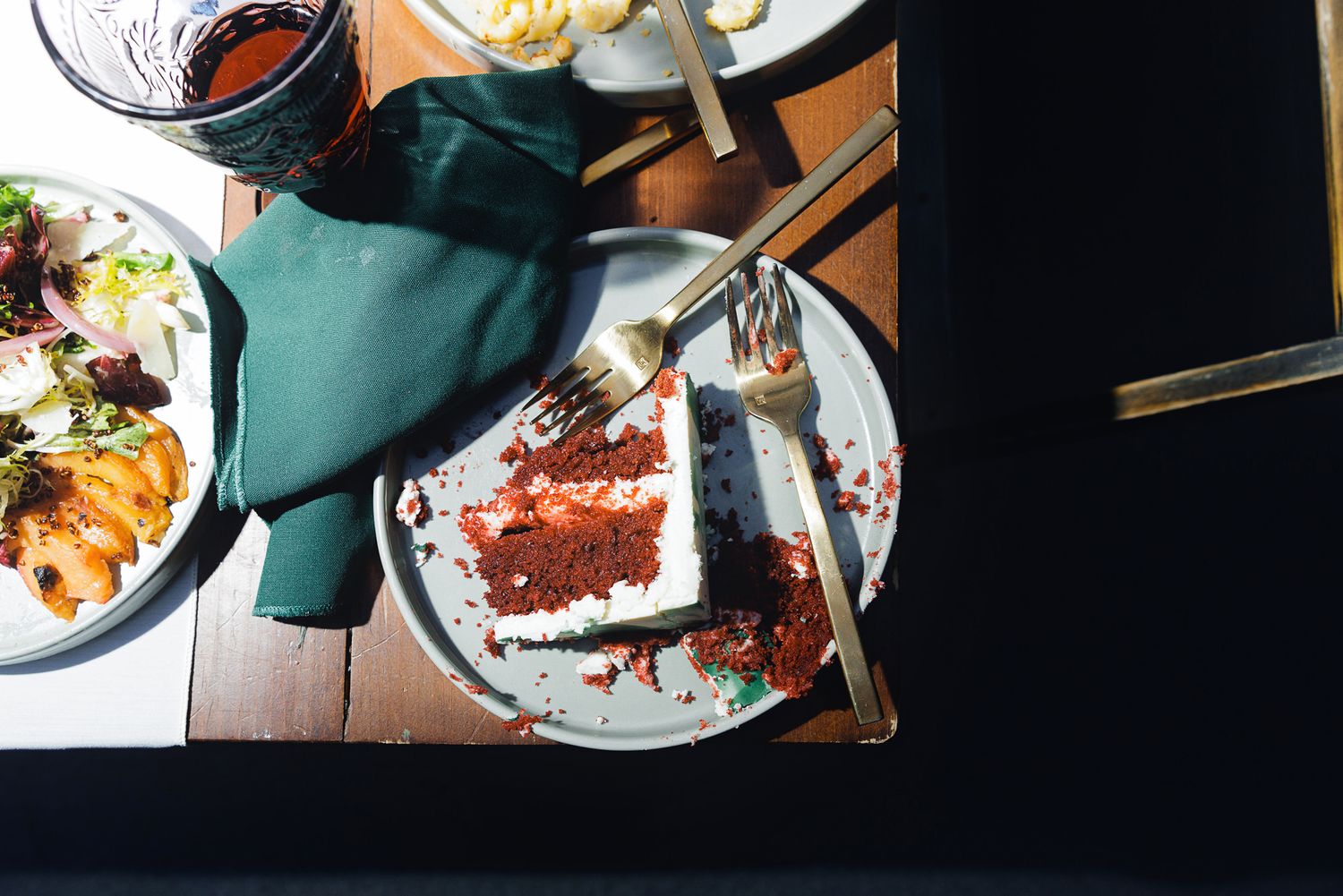 Overhead view of a partially eaten red velvet cake slice on a plate with fork and knife at a restaurant table.