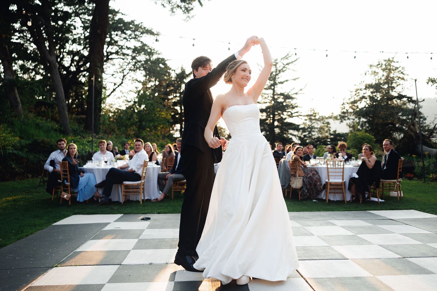 Bride and groom share first dance on checkered outdoor floor at elegant wedding reception.