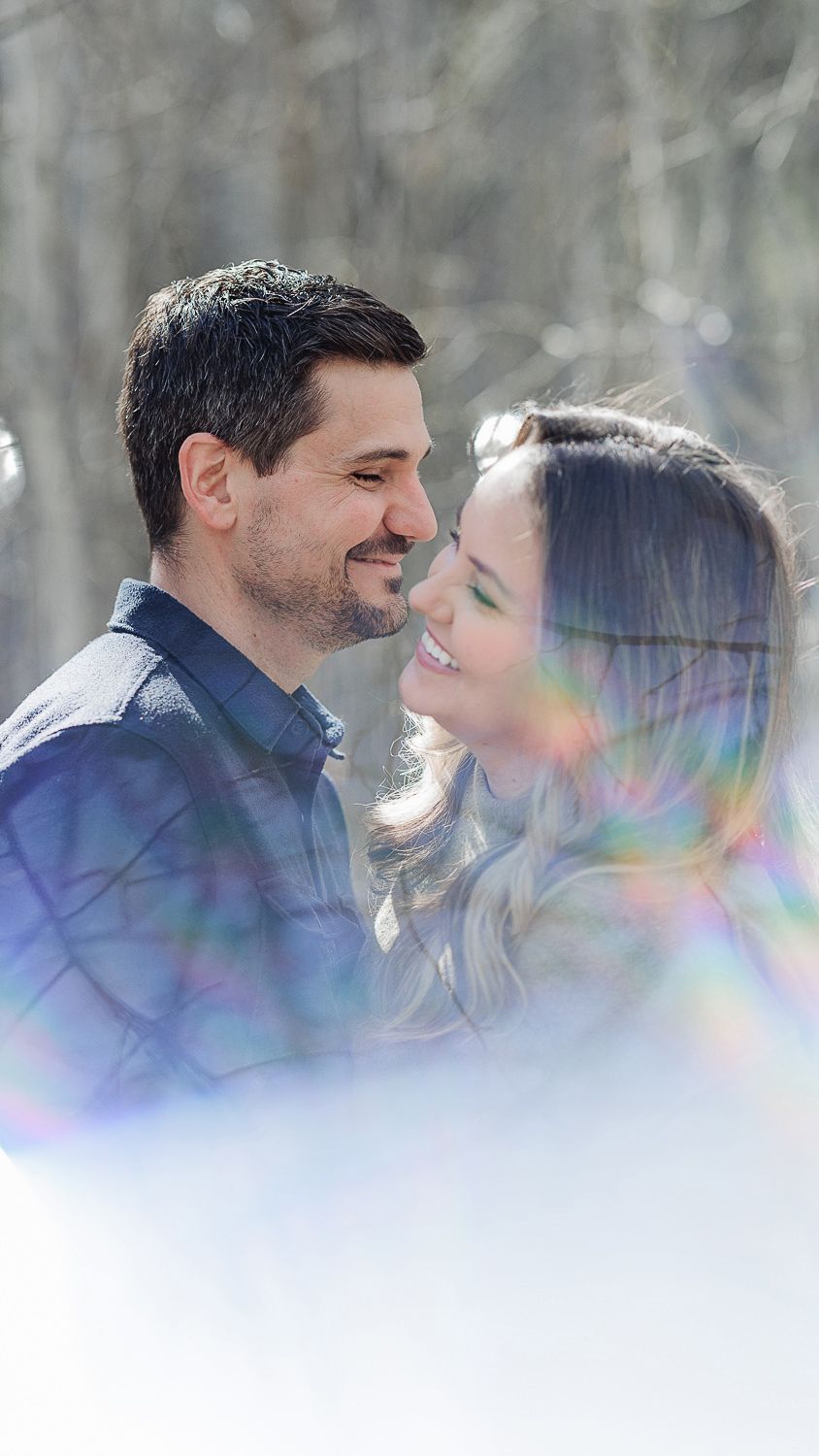A romantic couple shares an intimate moment in a snowy winter forest with dreamy lens flares and soft lighting.