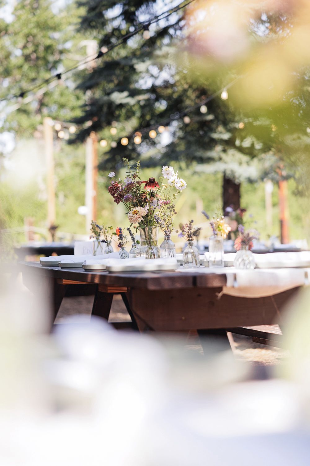 Elegant outdoor table setting with delicate floral centerpieces and place settings viewed through a soft focus foreground.