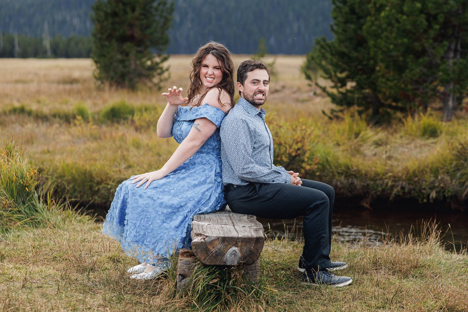 A couple sits together on a log in a scenic mountain meadow during a sunny autumn day.